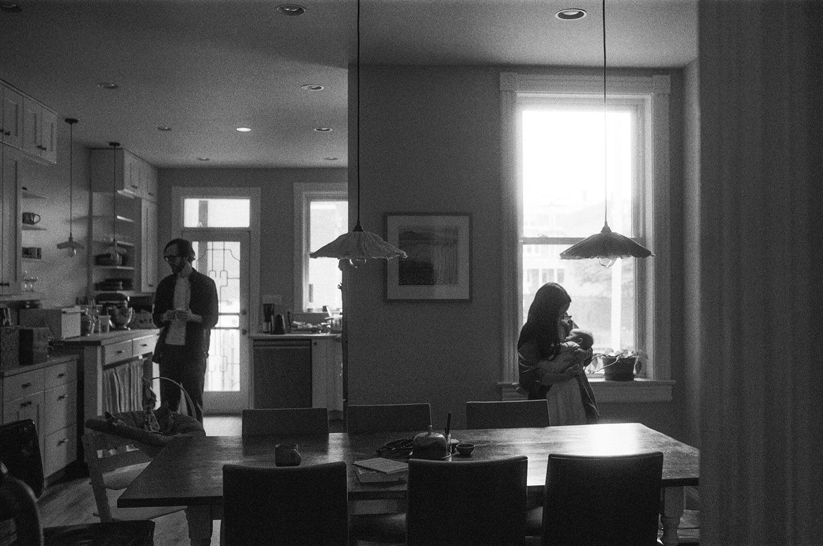 parents being lit in separate sides of the room by window light during a newborn session on film in the DMV 