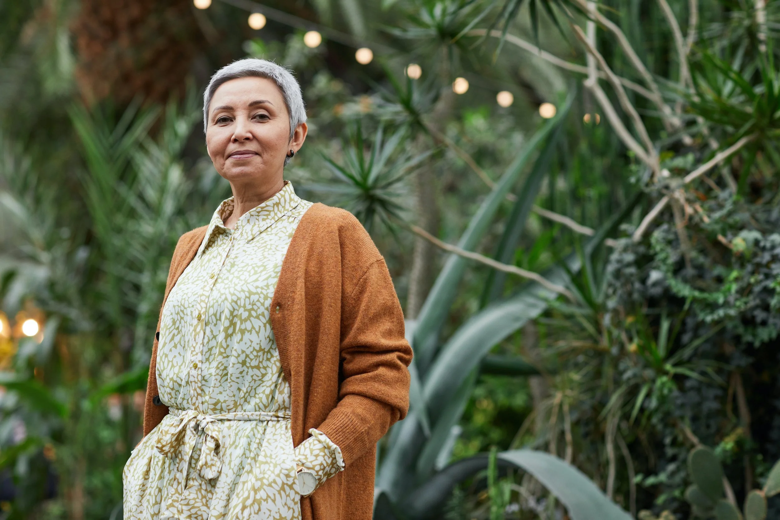 An older woman smiling while standing in front of foliage