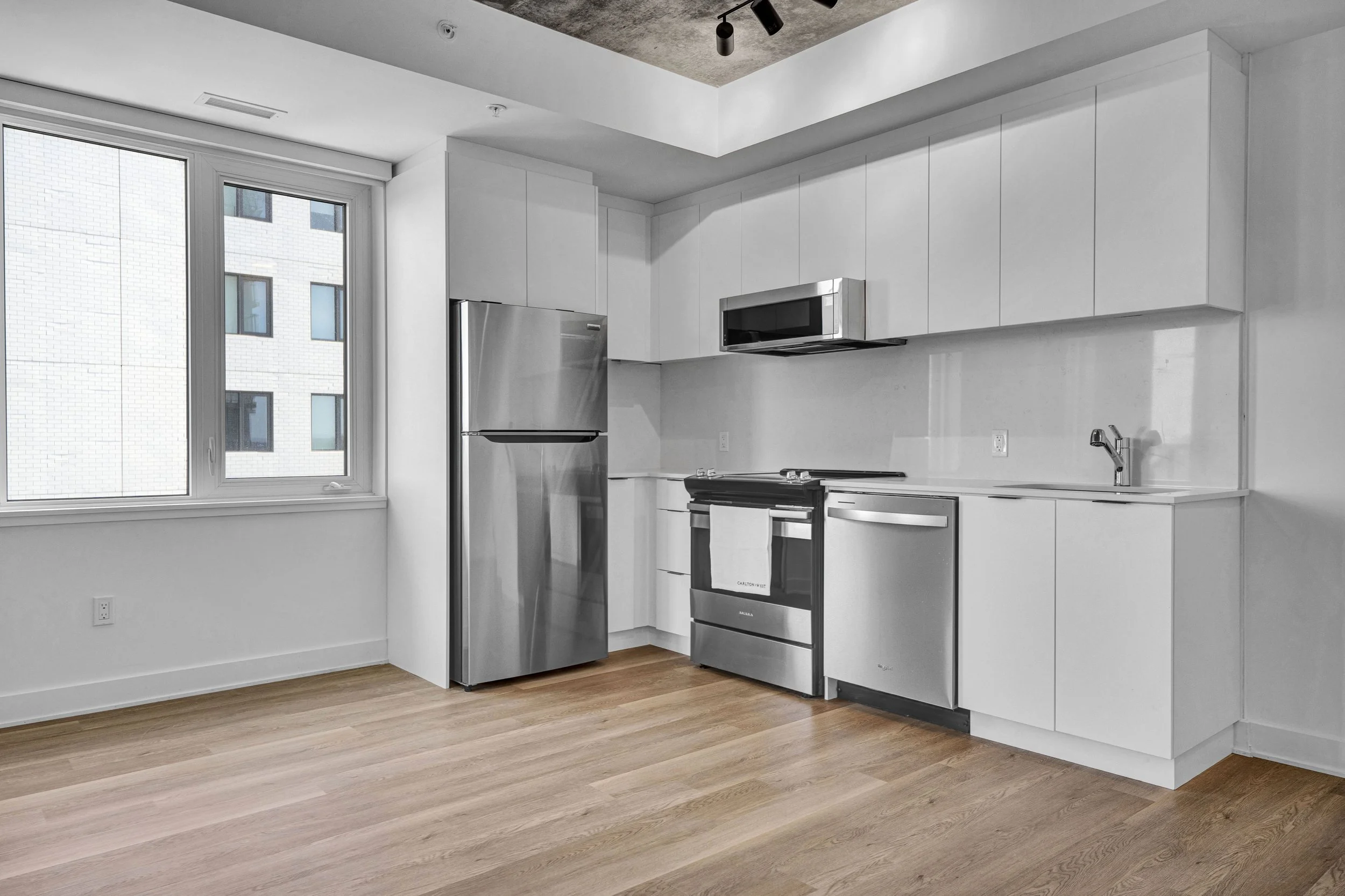 Modern kitchen with white cabinets, stainless steel appliances, a window, and wood flooring.