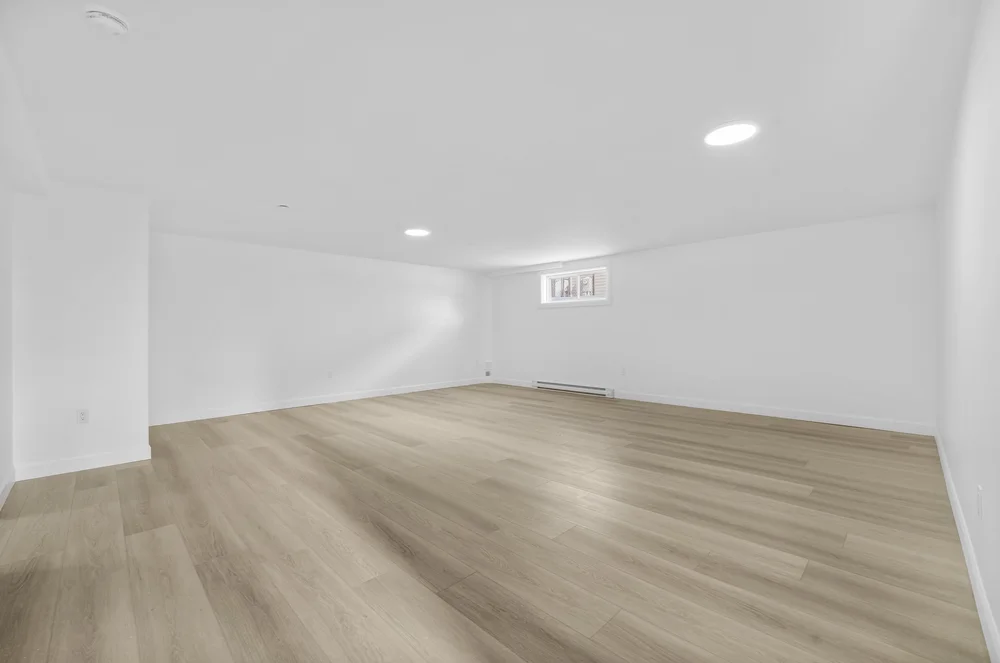 Original photo of an empty basement living area with wood flooring and a low window