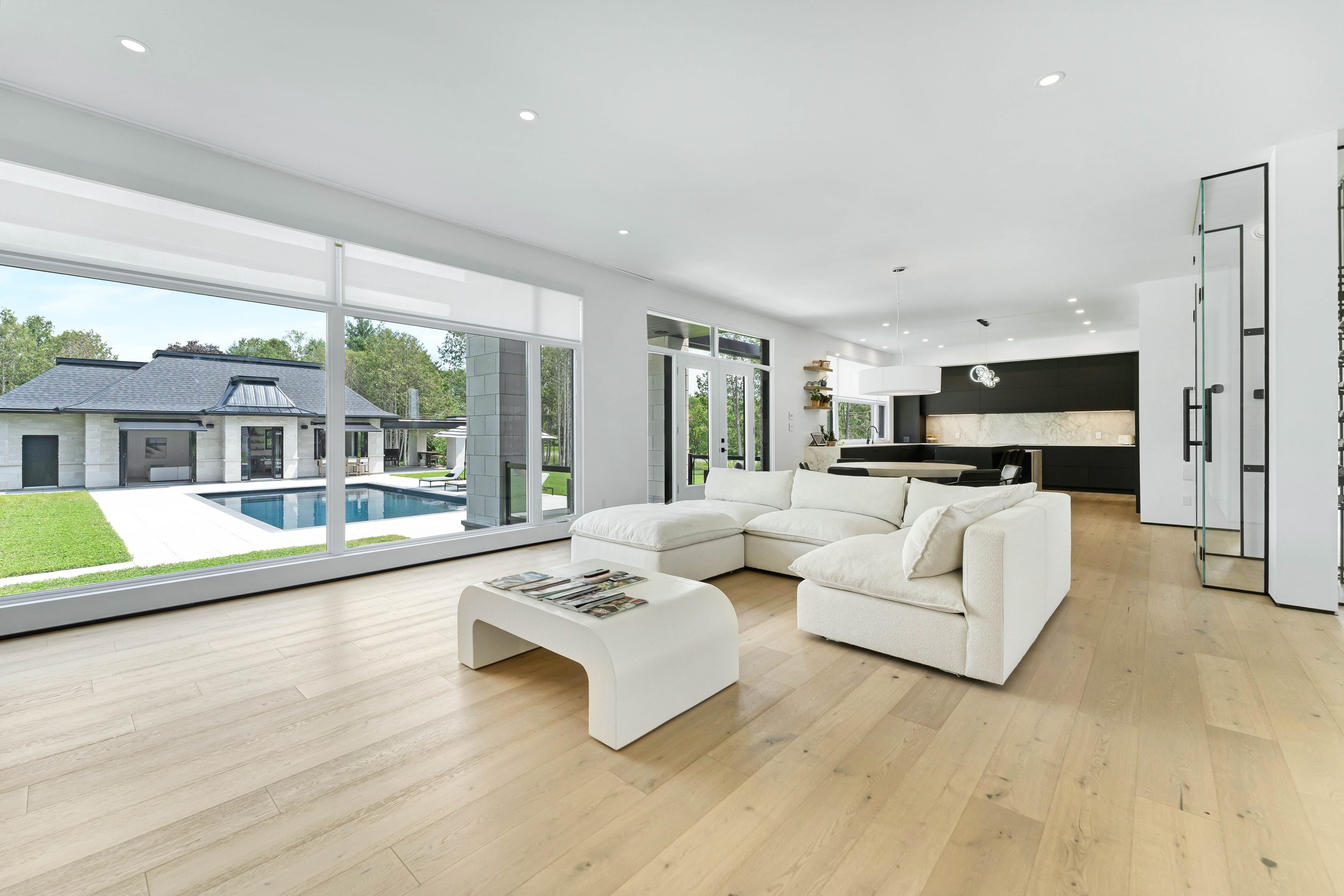 Modern living room with white sofa, wooden floor, glass doors opening to a pool and outdoor view, minimalistic design.
