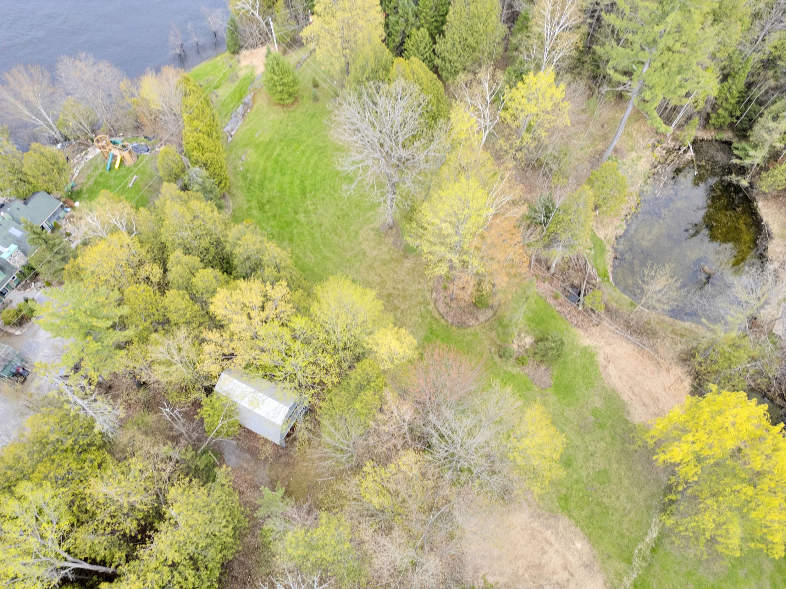 Ottawa Real Estate Media Services  An aerial view of a green lawn with scattered trees, a small pond, and some houses and a playground in a suburban neighborhood.
