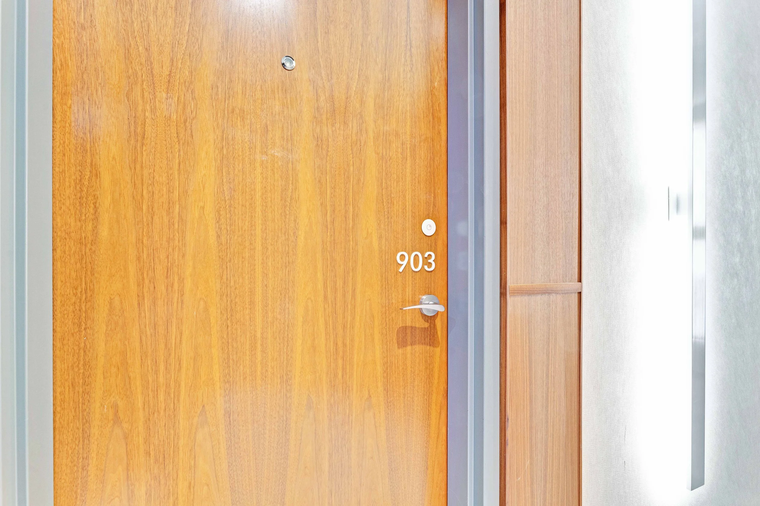 NV3D Ottawa Real Estate Photography Wooden door with the number 903, a peephole, a door handle, and a doorbell, surrounded by a frame and partially visible wall.