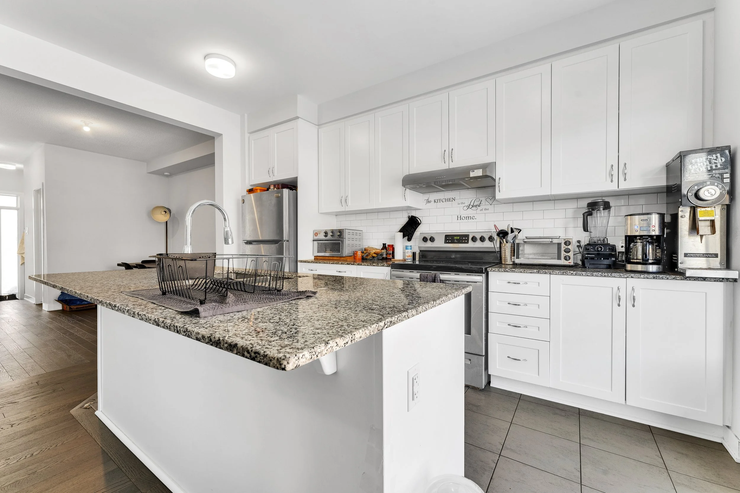 Modern kitchen with white cabinets, granite countertops, stainless steel appliances, and various small appliances on the counter.