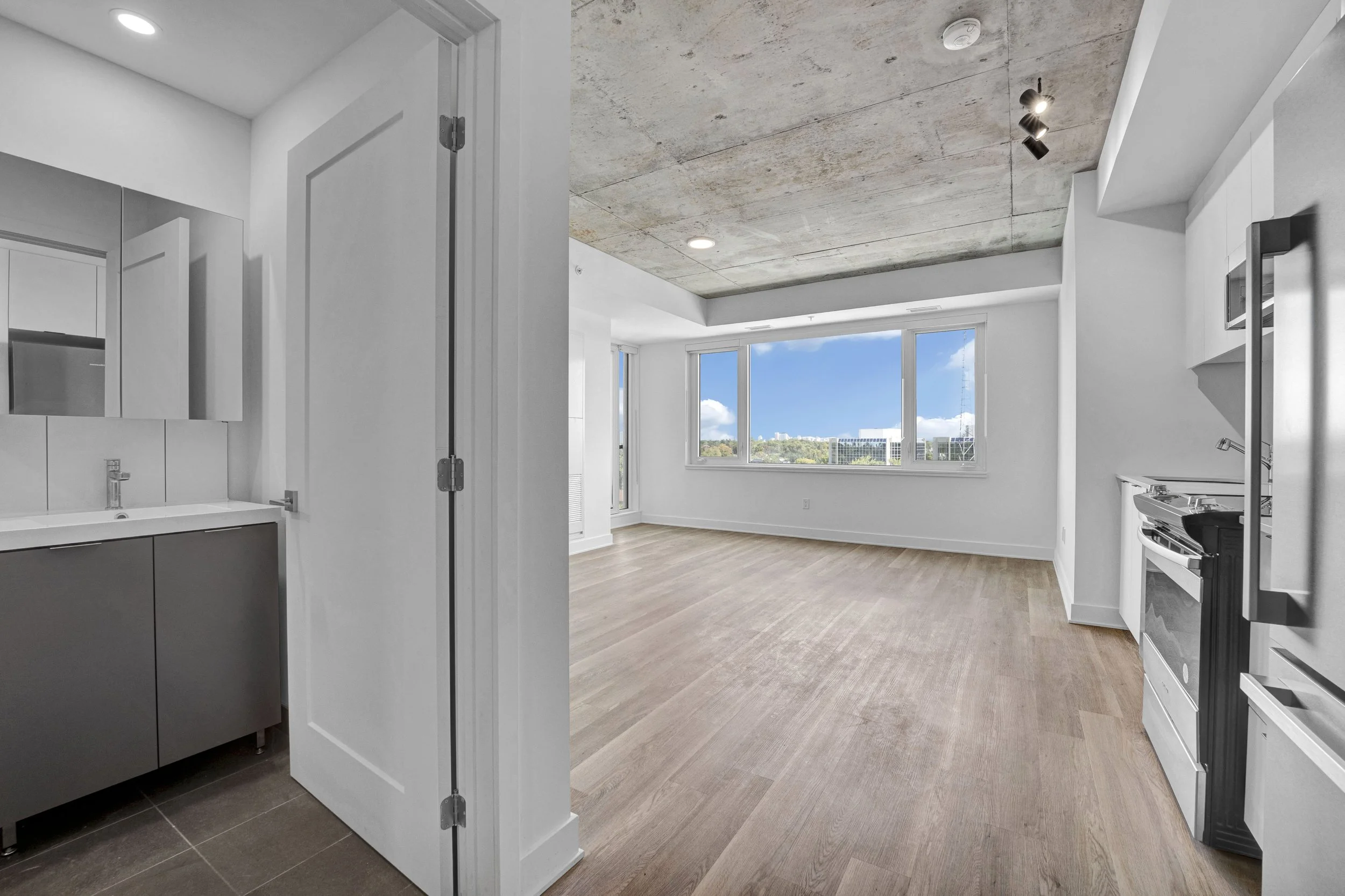 Modern apartment with view of city and sky, featuring a kitchen with light wood flooring, large windows, and minimalist design elements.