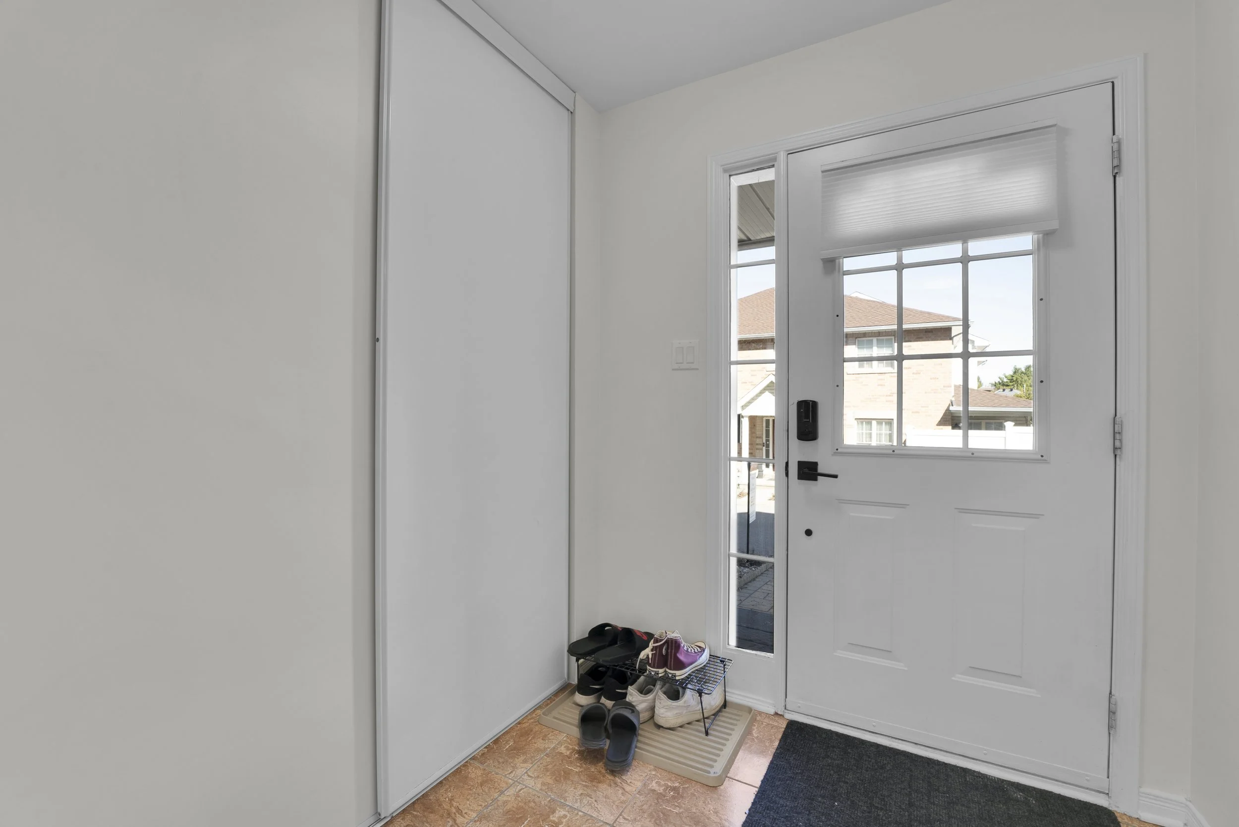 NVISION3D.ca Real Estate Media Ottawa  Entryway with white door leading outside, shoes on a shoe rack, and a sunlit view of neighboring houses through the window.
