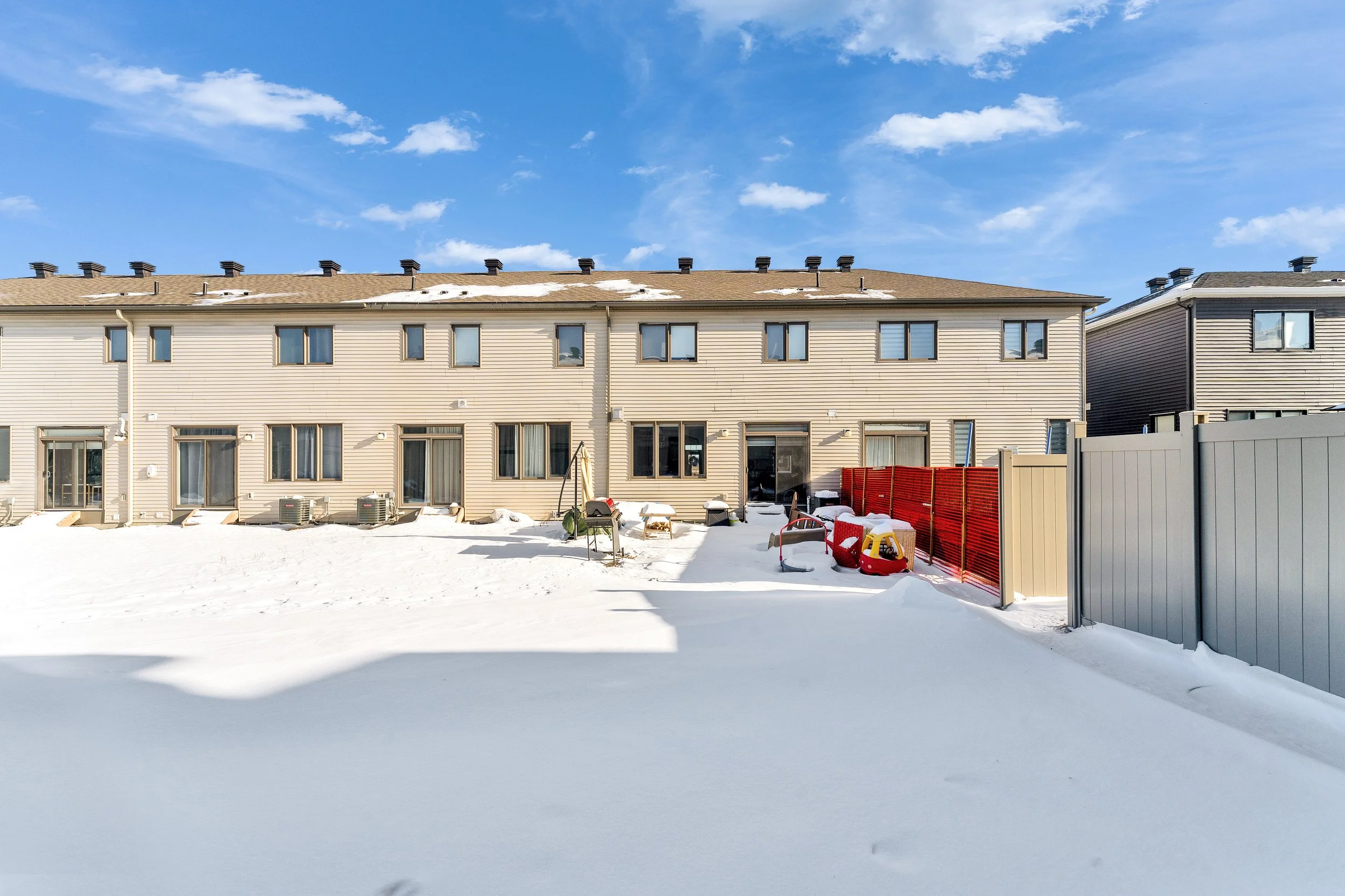 NV3D Real Estate Photography Ottawa  Backyard of a row of beige townhouses covered in snow, with a blue sky and few clouds.
