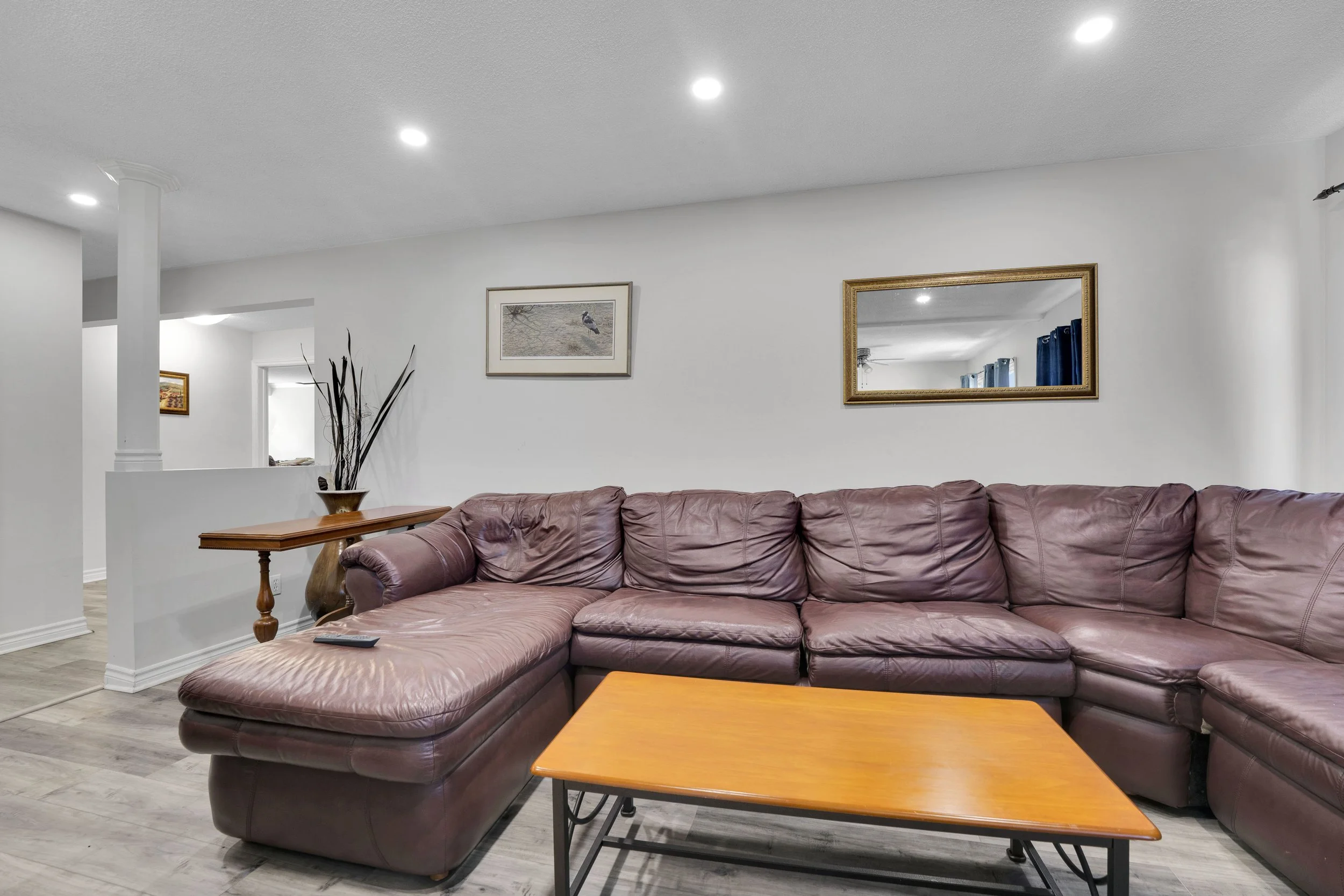 Ottawa Real Estate Media Services  Living room with purple sectional sofa, wooden coffee table, framed pictures on the white wall, a mirror, and a corner with tall decorative branches.