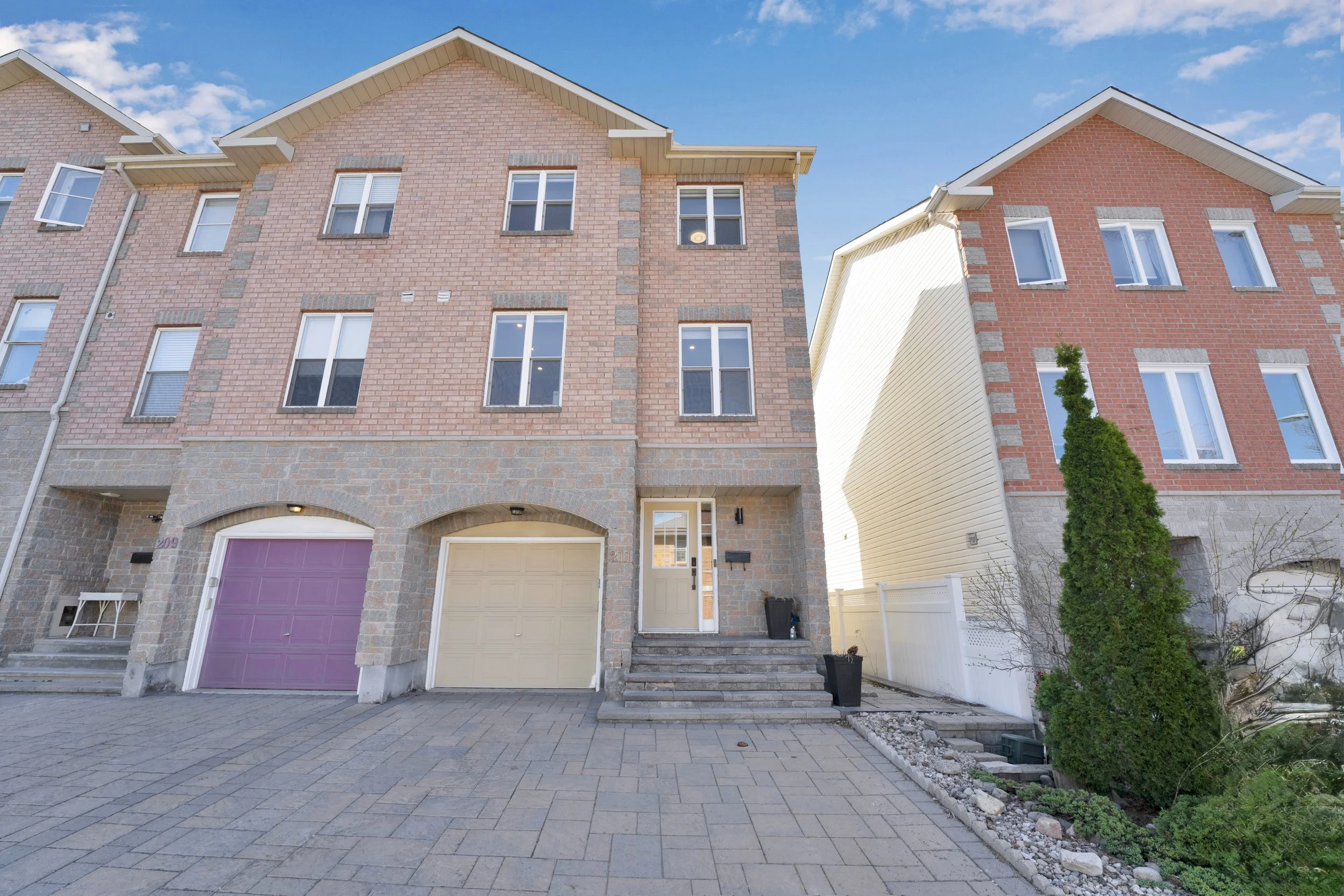 NVISION3D.ca Real Estate Media Ottawa  Front view of two neighboring modern townhouses with brick facades, paved courtyard, small garden, and bright blue sky.