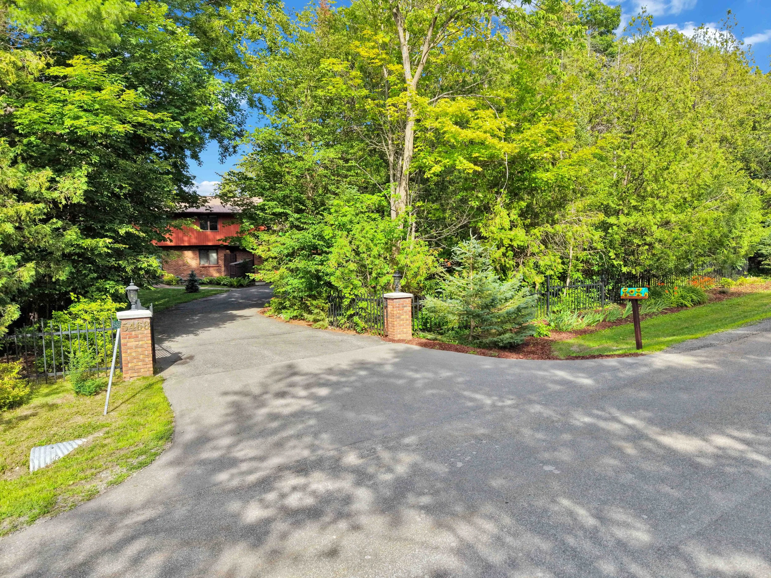NVISION 3D Real Estate Media  A paved driveway leading to a house surrounded by lush green trees and a well-maintained lawn.