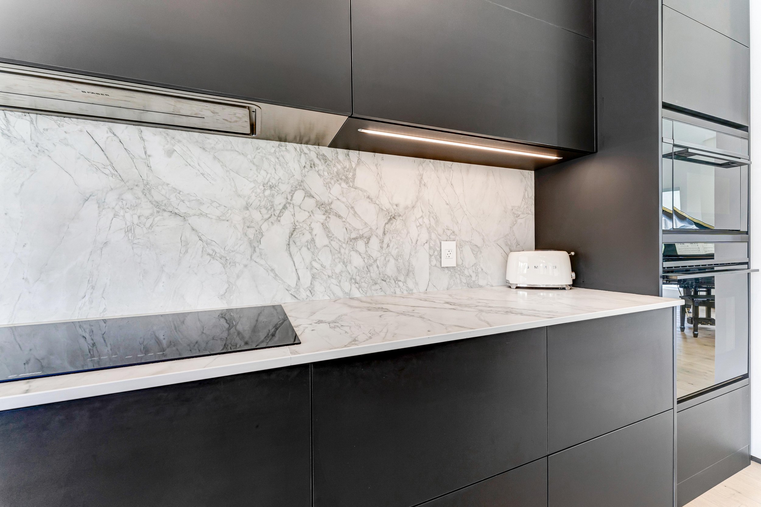 Modern kitchen with marble countertop, backsplash, black cabinets, white toaster, and sleek cooktop.