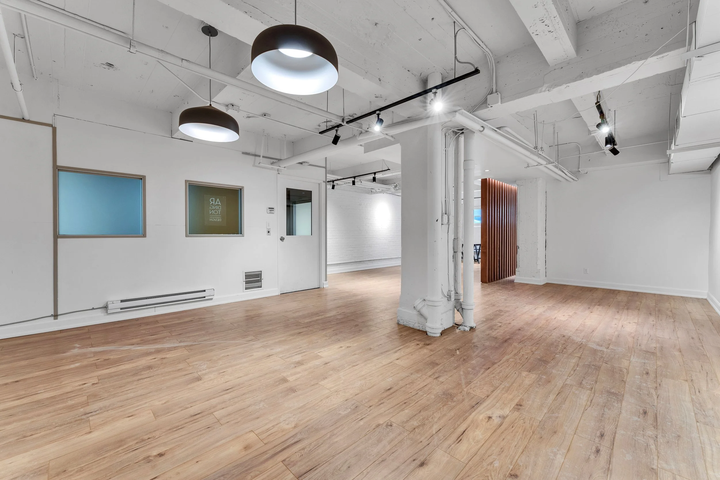 photographie immobiliere outaouis  Empty interior space with white walls, wooden flooring, exposed ceiling pipes, and modern light fixtures.