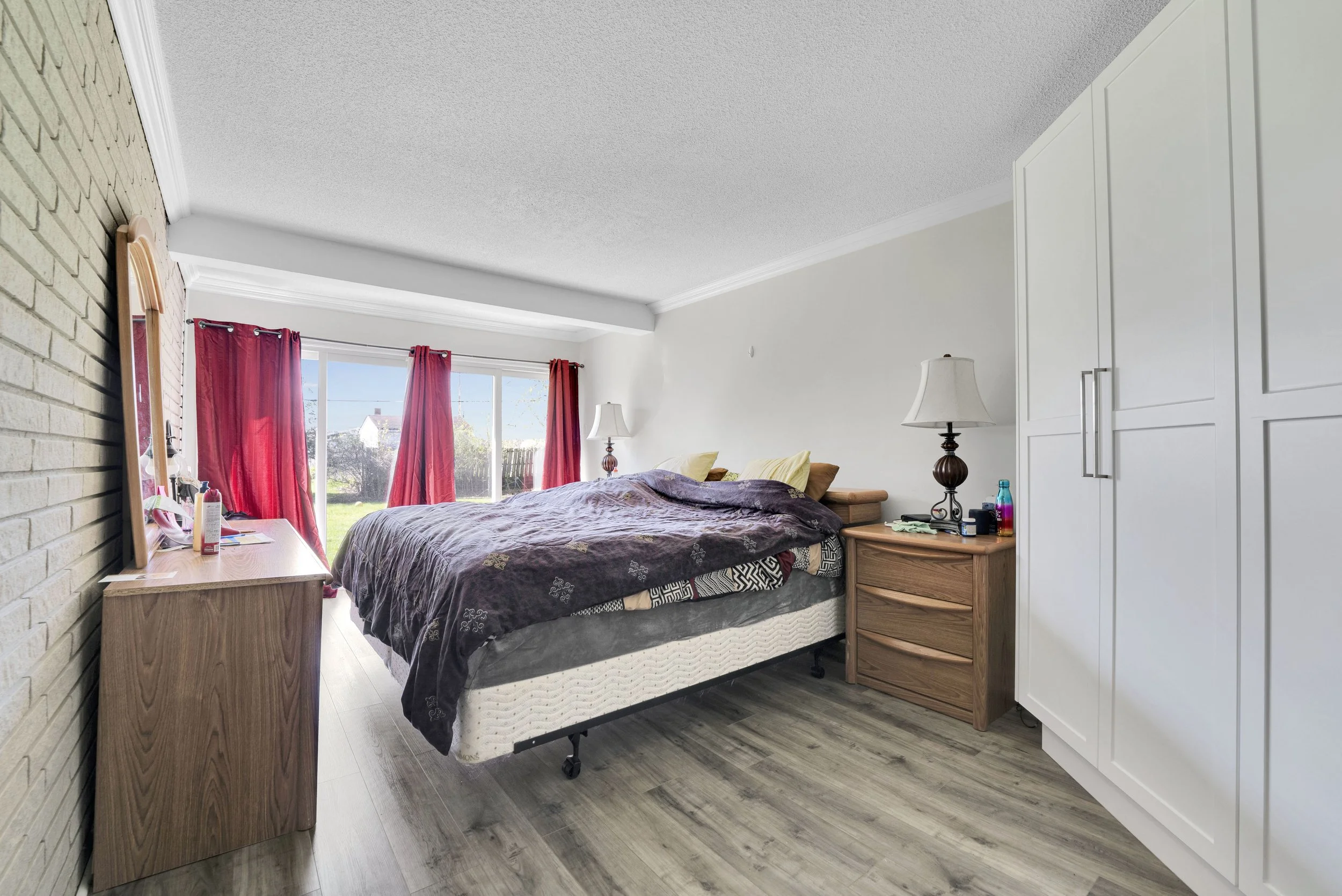 Ottawa Real Estate Media Services  A bedroom with a bed, bedside table, lamps, window with red curtains, and a white wardrobe