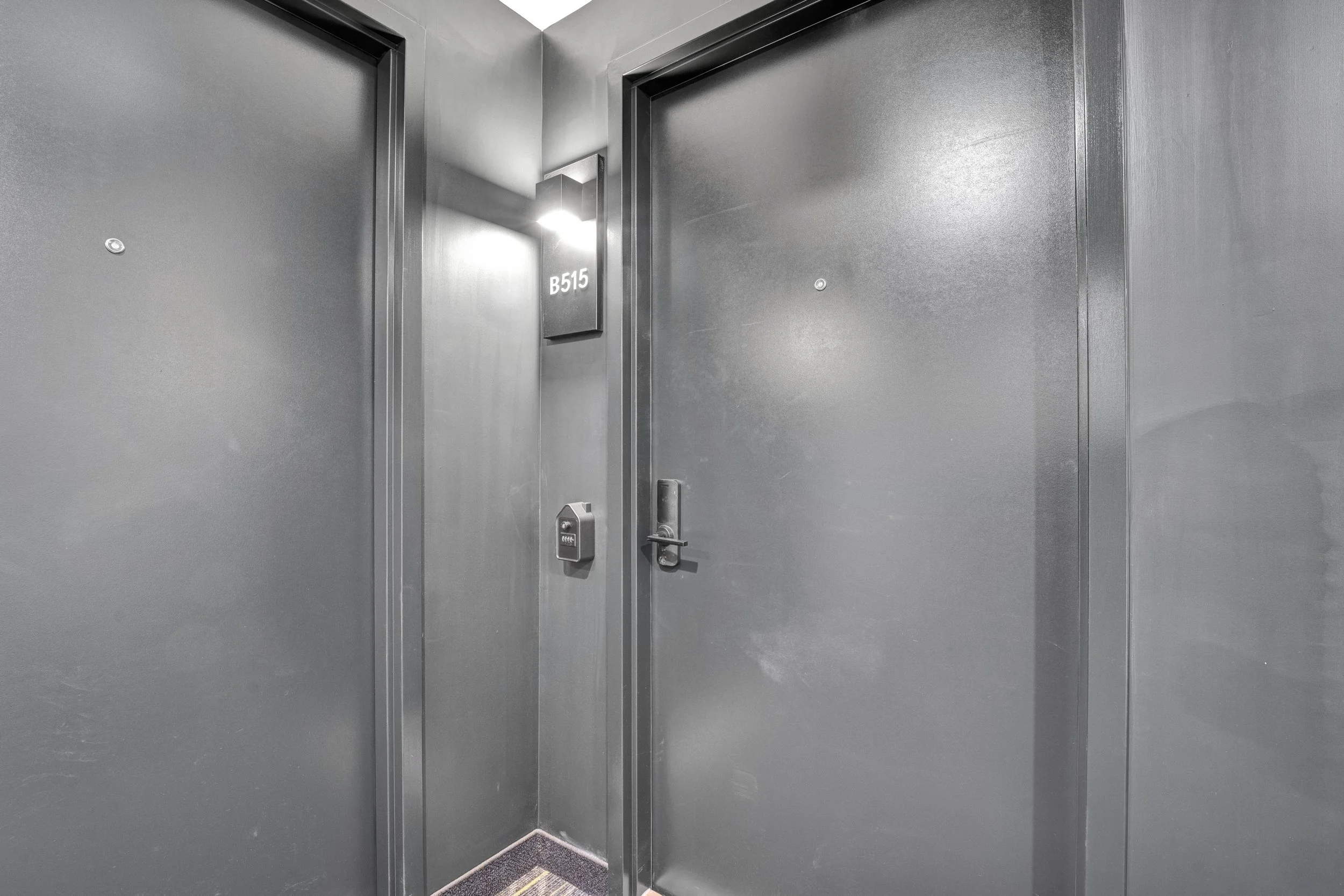 Ottawa Real Estate Photographer A gray hallway with two closed elevator doors, a wall-mounted light fixture, and a sign that reads 'B515' near the light.