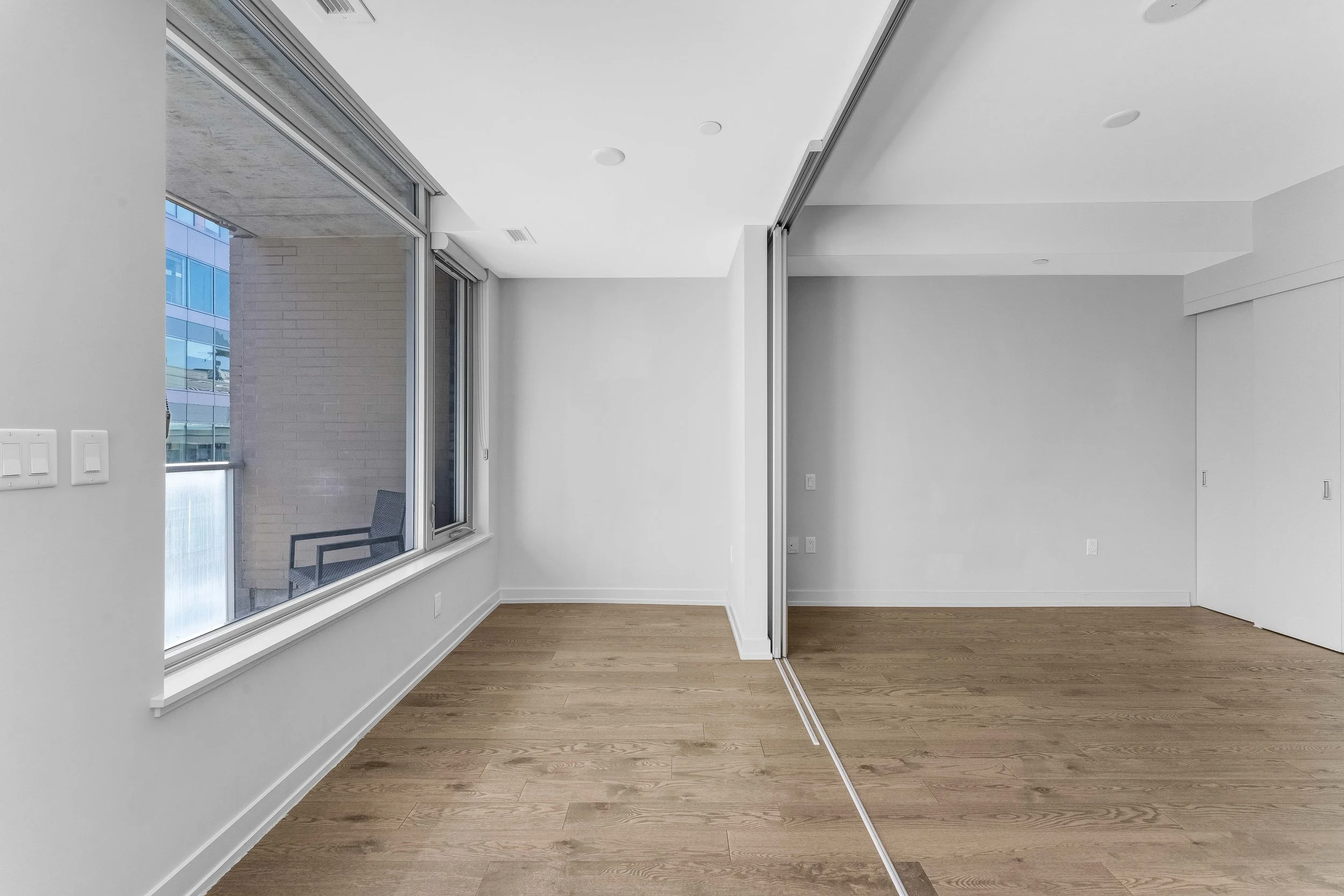 NV3D Ottawa Real Estate Photography Empty modern apartment room with large window, hardwood floors, and sliding closet doors.