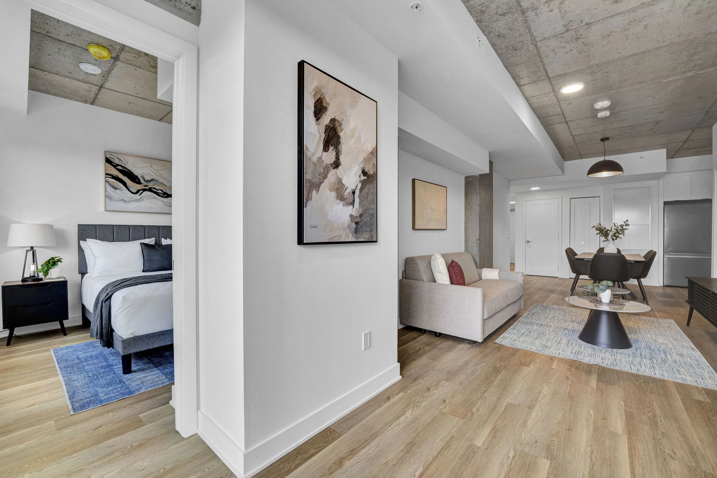 Ottawa Real Estate NVISION 3D  Living room with beige sofa, wall art, dining table with chairs, and modern decor in an apartment with wooden floors and industrial ceiling.