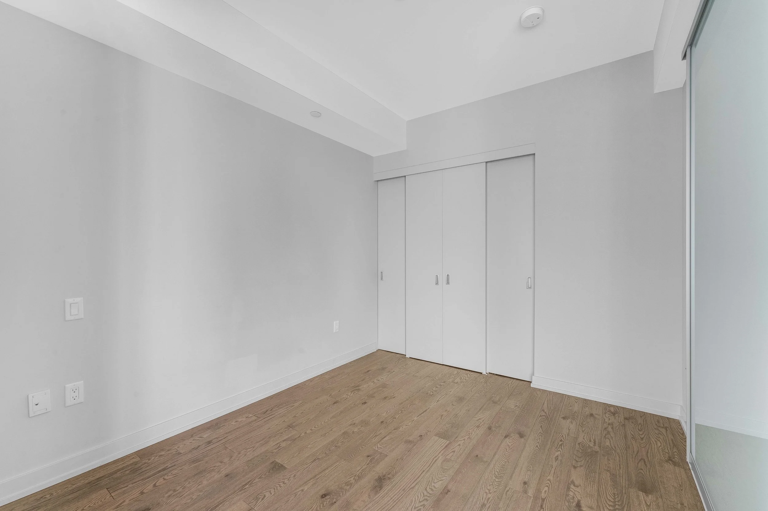 NV3D Ottawa Real Estate Photography Empty room with white walls, wood flooring, and a closet with sliding doors.