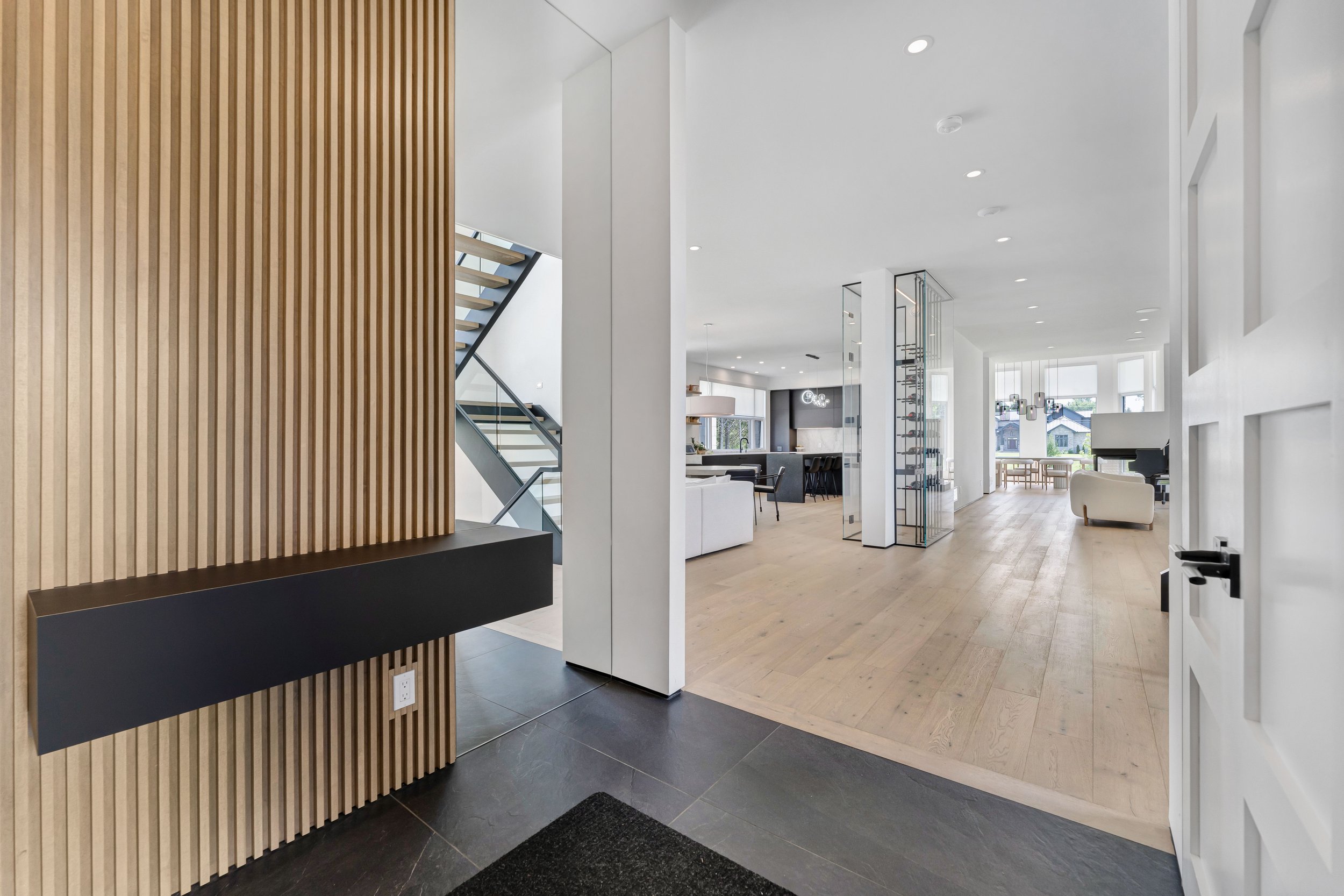 Modern open-plan living area with wooden flooring, staircase, and wood panel accent wall.