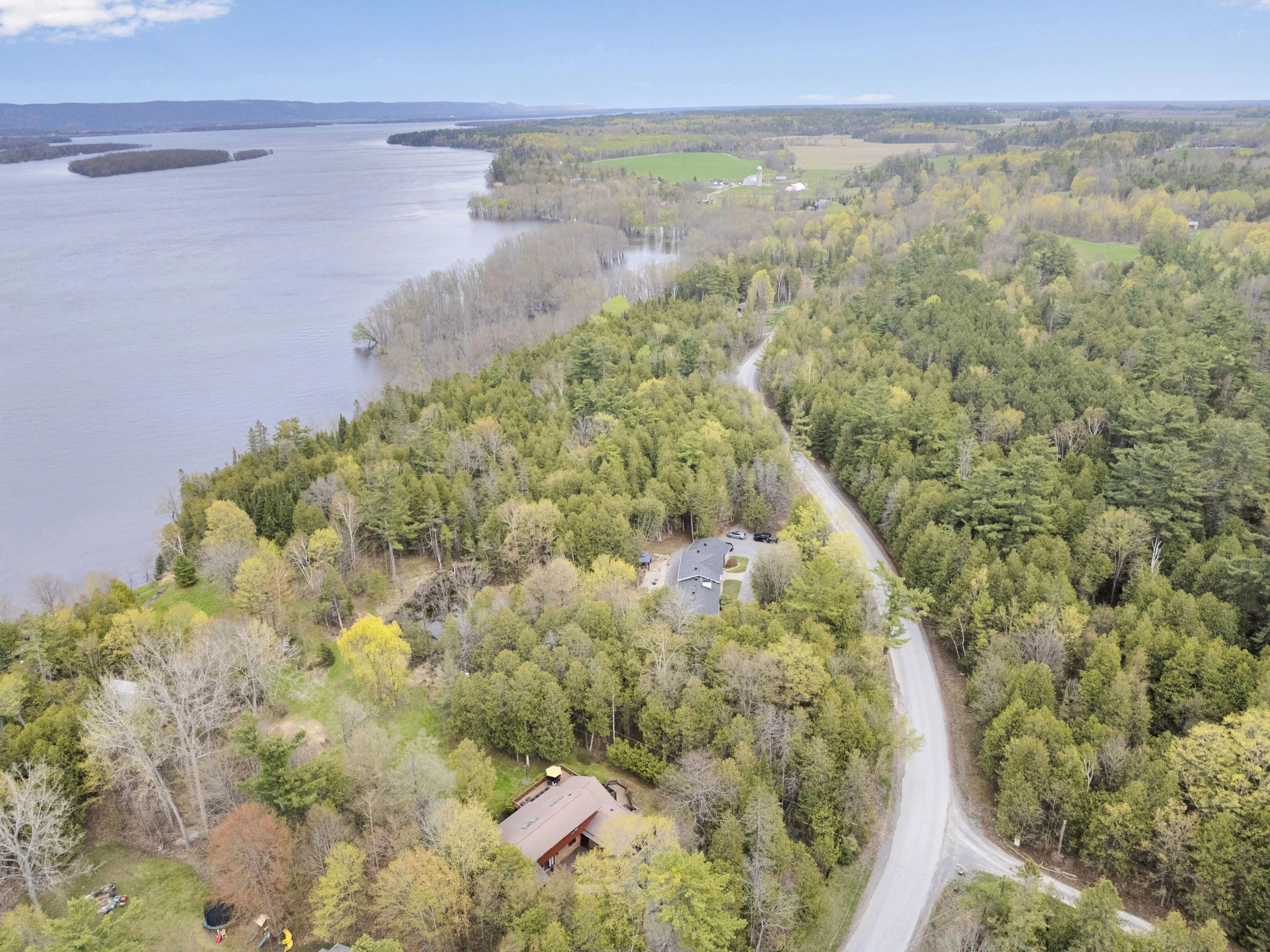 NVISION3D.ca Real Estate Media Ottawa  Aerial view of a river and surrounding landscape with trees, houses, and fields in the distance.