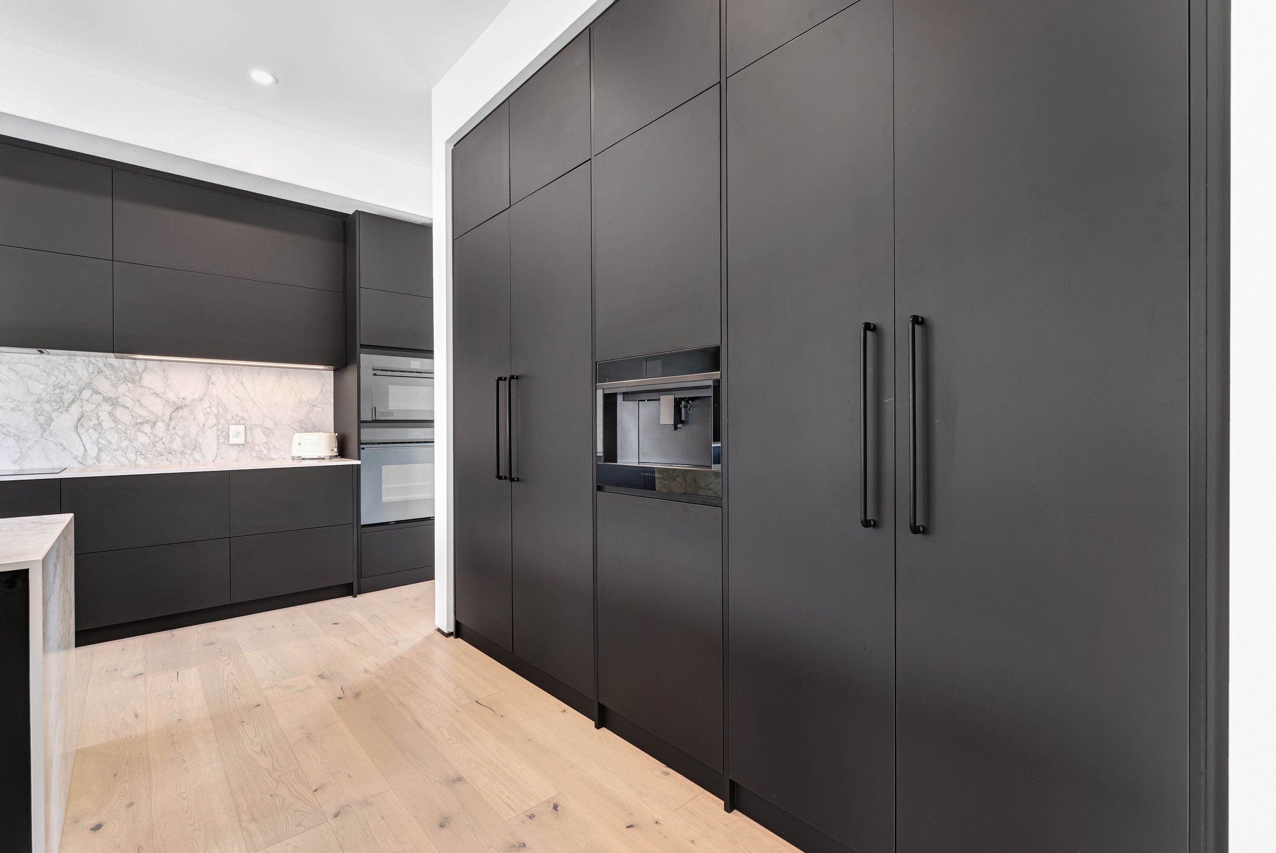 Modern kitchen with black cabinets, marble countertops, light wood flooring, and built-in appliances.