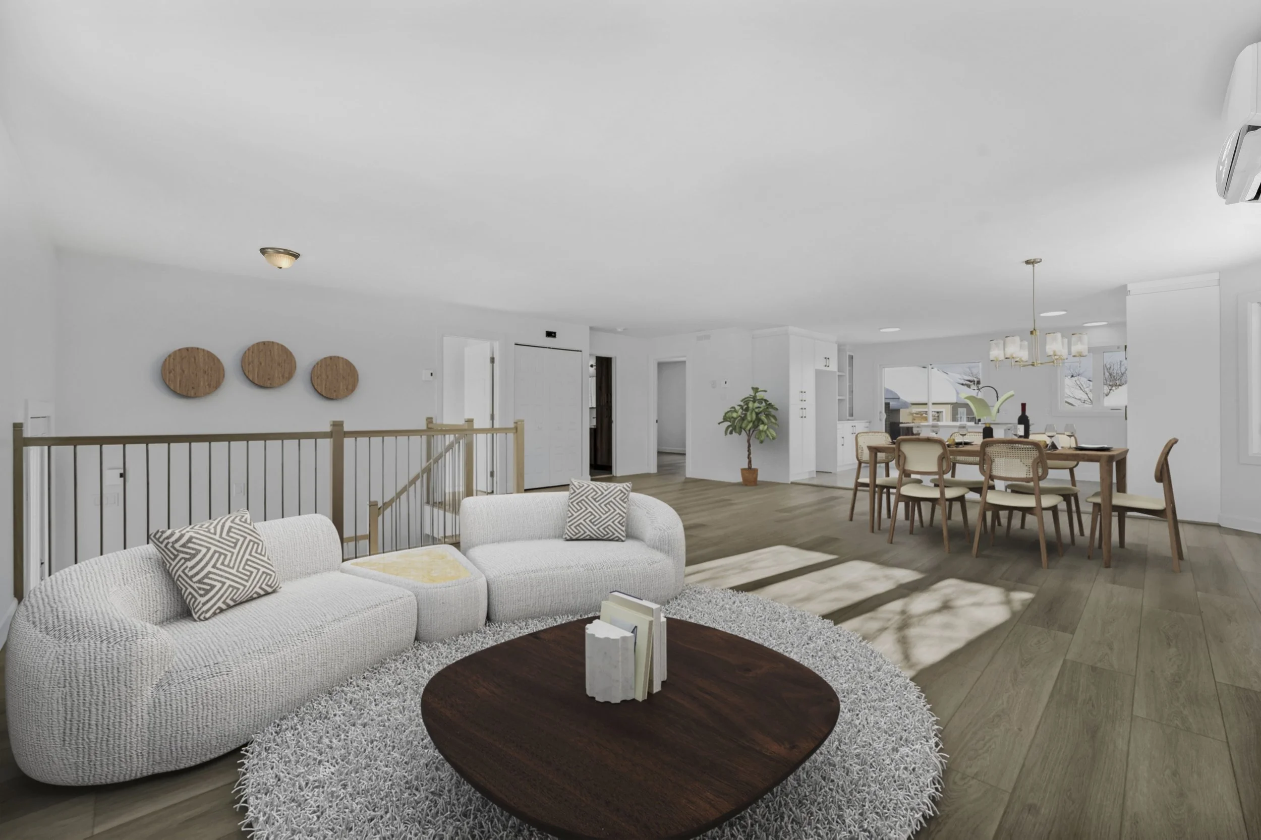 Bright, spacious living room and dining area with white walls, hardwood floors, white sectional sofa with patterned pillows, round wooden coffee table, and a dining table with eight chairs, illuminated by a chandelier, with a large window and potted 