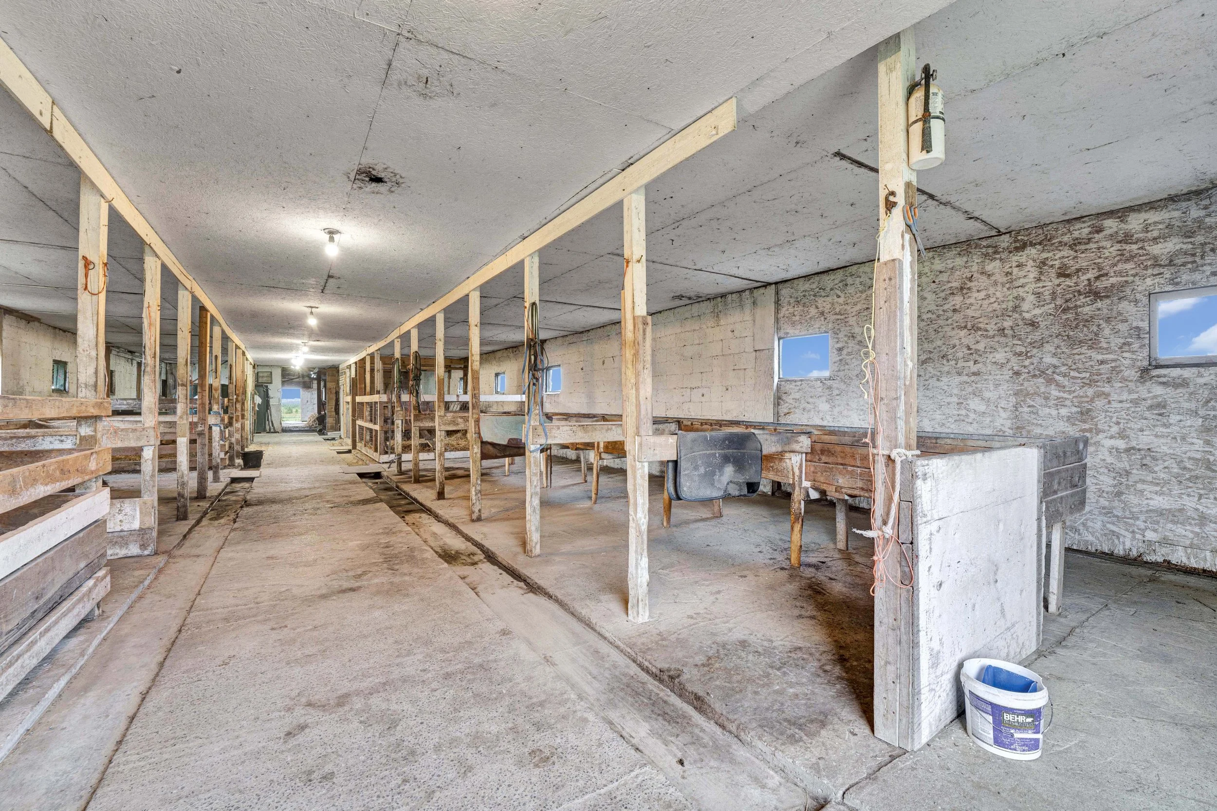 Interior of a building under construction with exposed wooden framing, concrete floors, and a partially finished ceiling with hanging light bulbs.