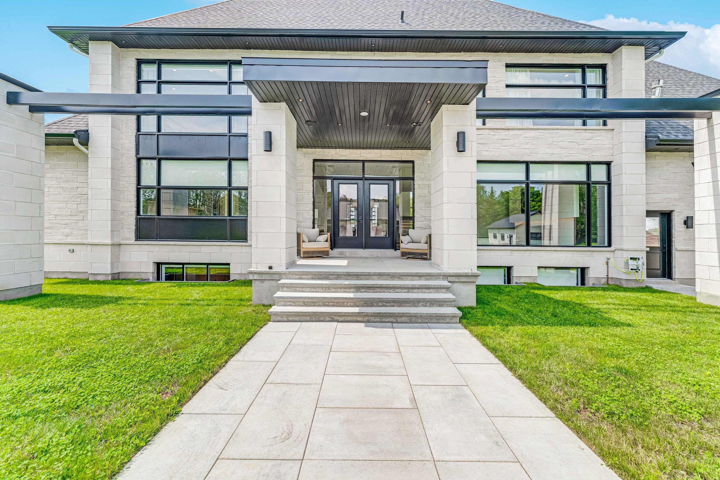 Modern house exterior with large windows, stone facade, and a covered entryway with steps leading up to double doors.