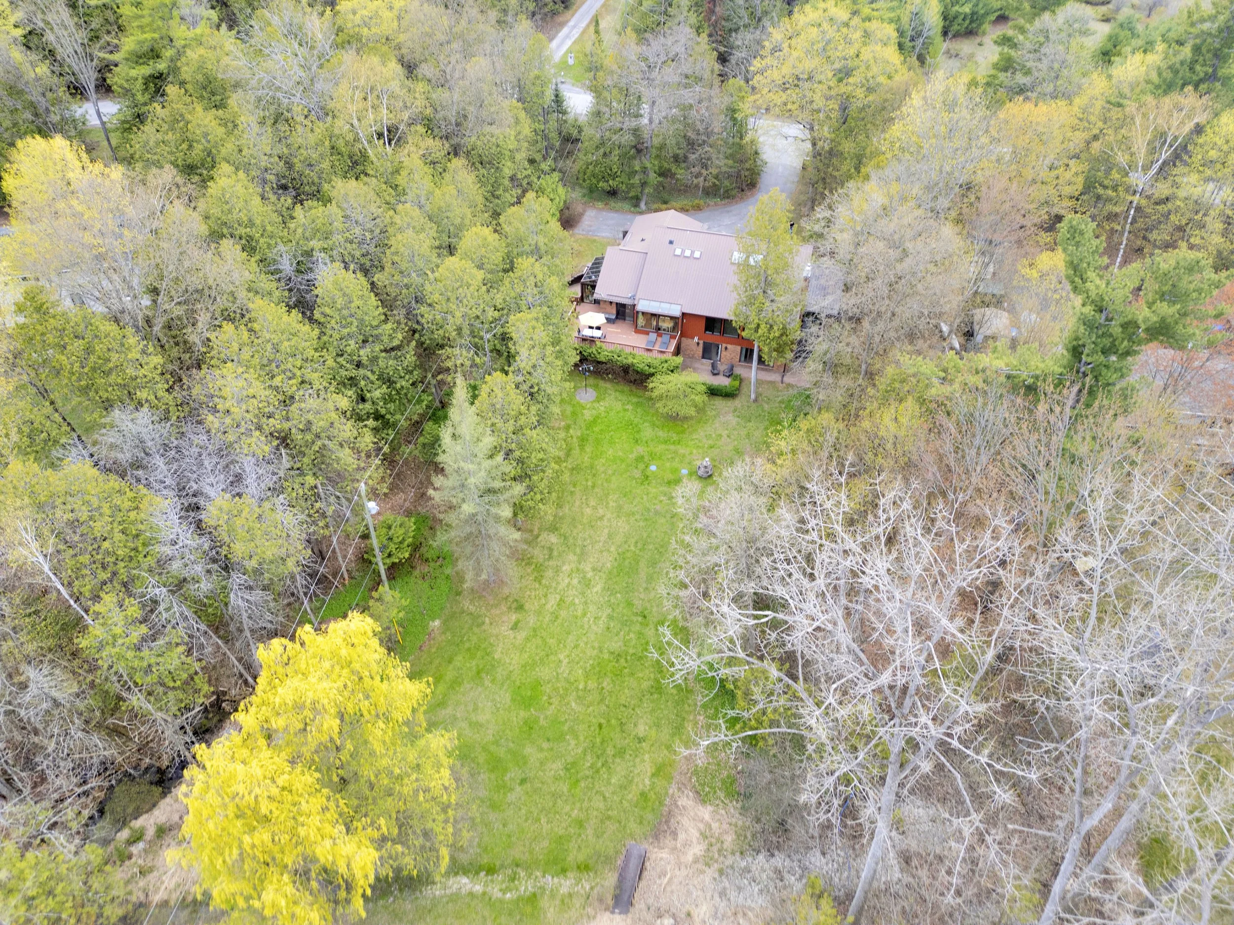 Ottawa Real Estate Media Services  An aerial view of a house surrounded by trees and greenery, with a driveway and a manicured lawn.