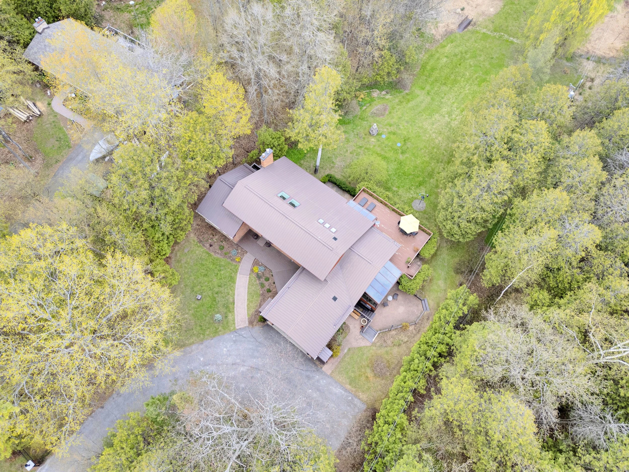 Ottawa Real Estate Media Services  Aerial view of a house surrounded by trees and greenery, with a driveway and a backyard with a flagstone patio and outdoor furniture.
