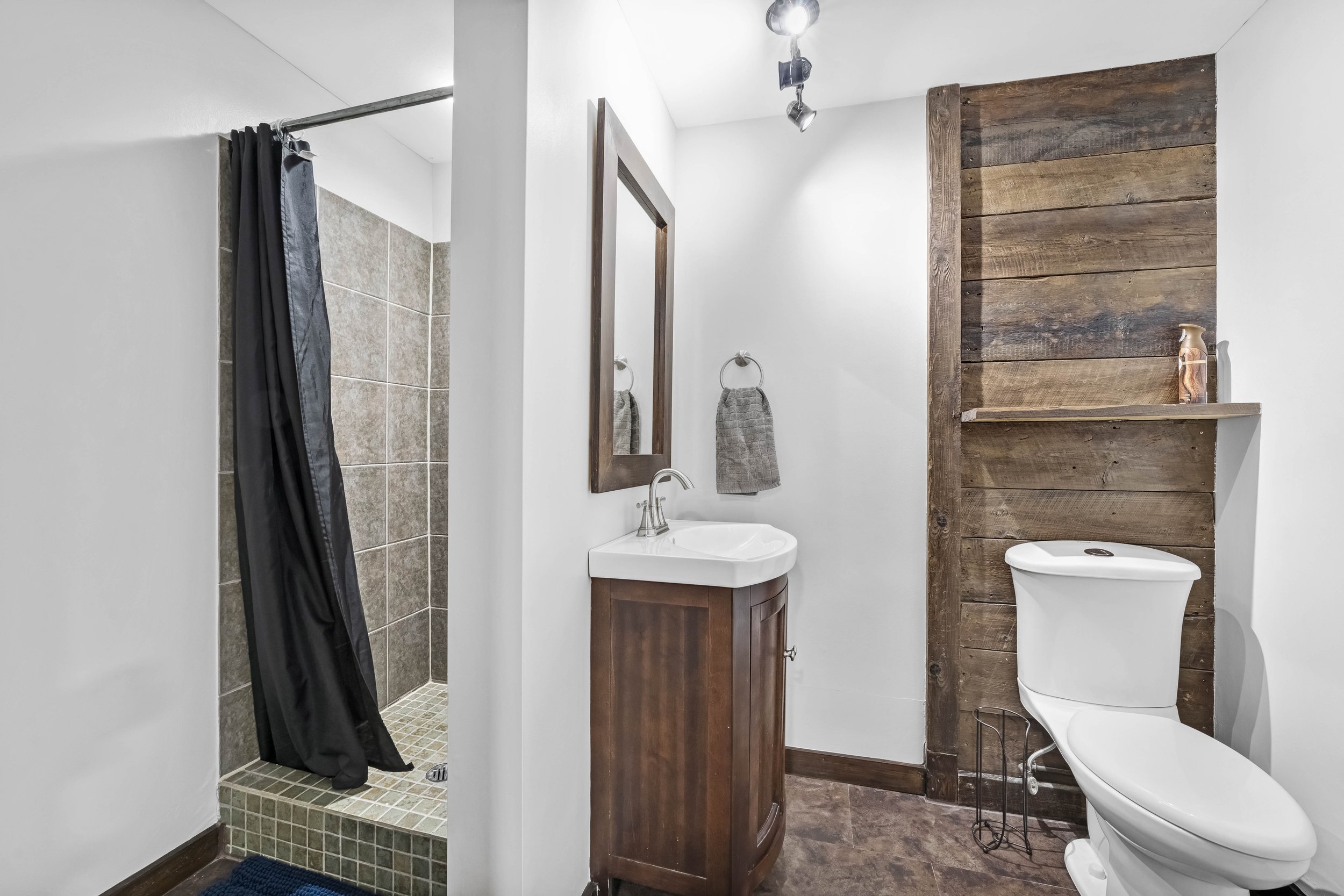 Bathroom with shower, pedestal sink, mirror, towel, wooden wall accents, and toilet.