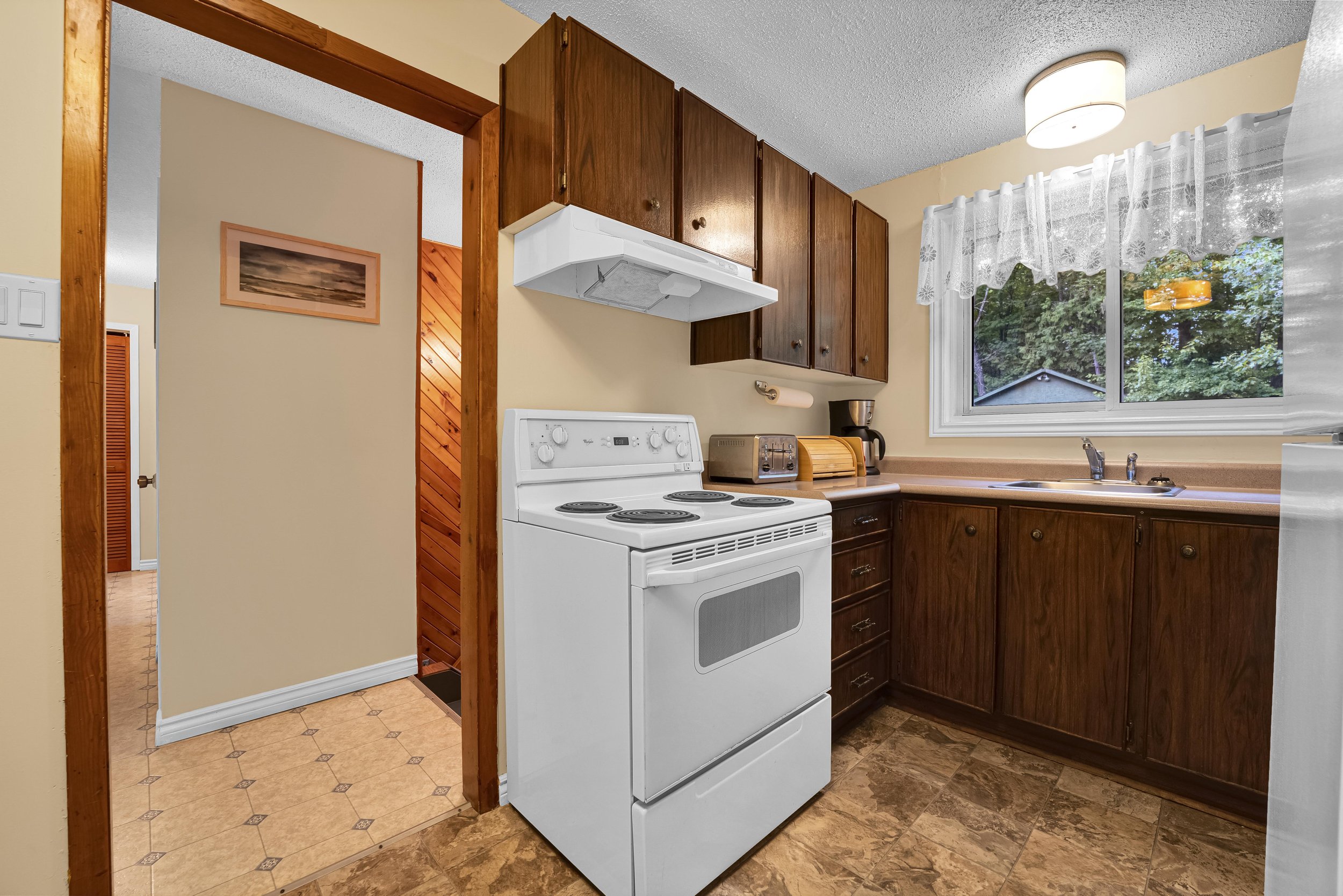 Ottawa Real Estate Photographer A kitchen with a white stove, wooden cabinets, and a large window with lace curtains.
