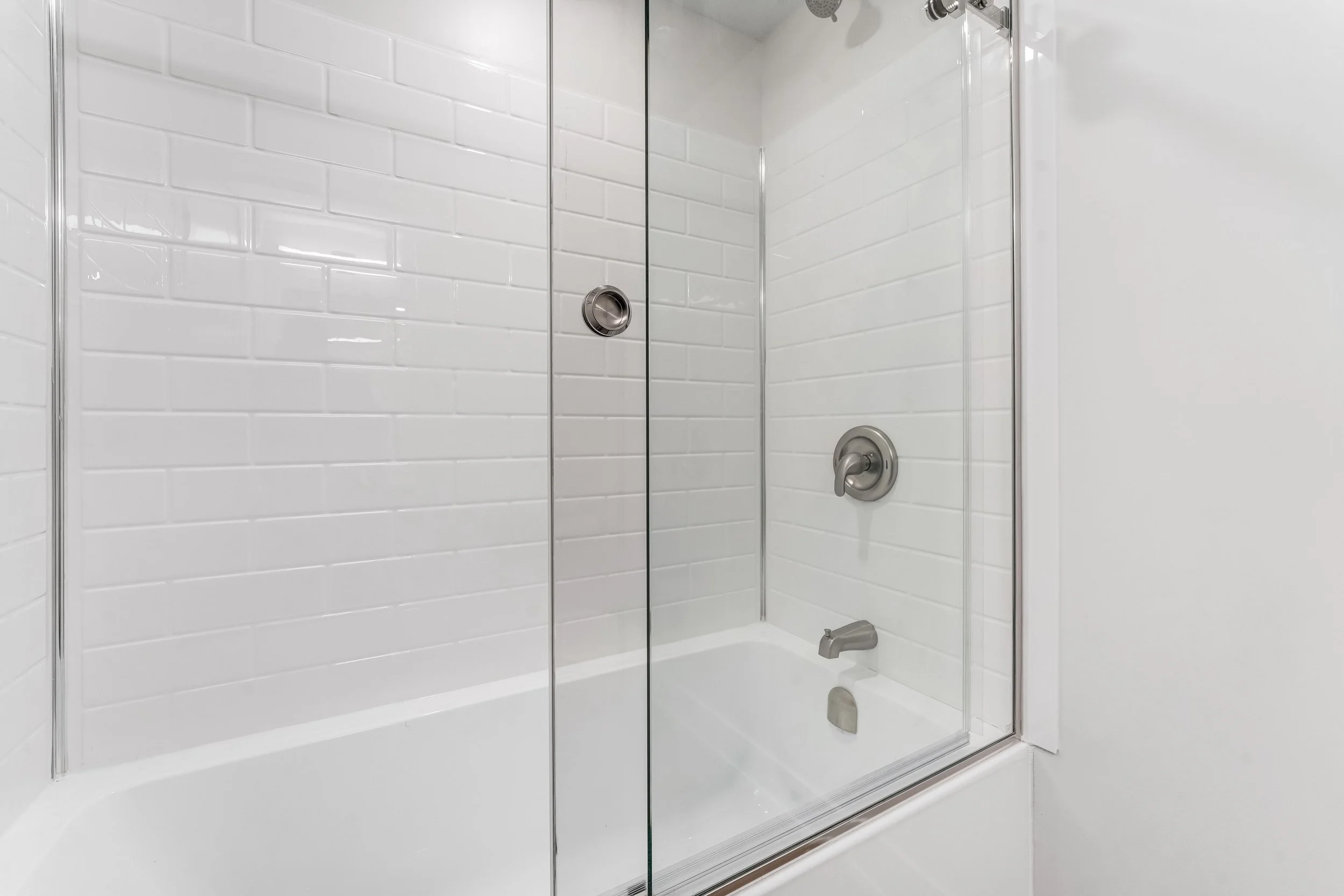 Empty walk-in shower with white subway tile walls, glass door, and stainless steel fixtures.