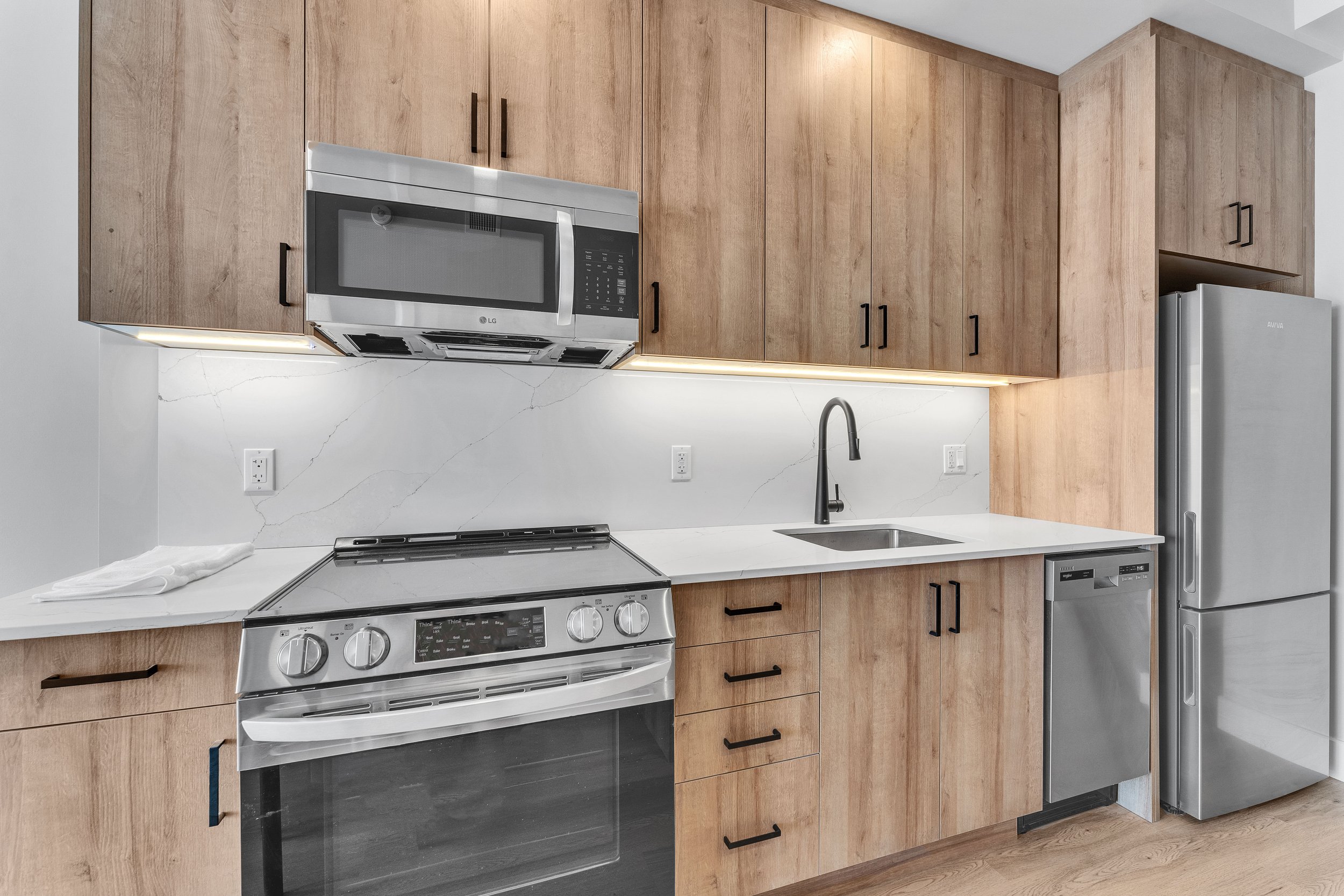 Modern kitchen with wooden cabinets, stainless steel appliances, and a white marble backsplash.