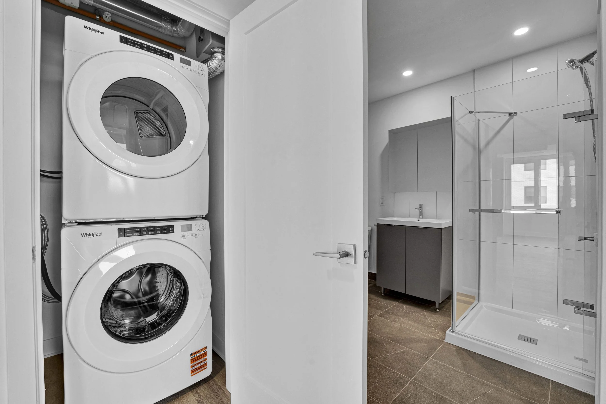 A laundry room with a stacked washer and dryer and a bathroom with a shower and sink.