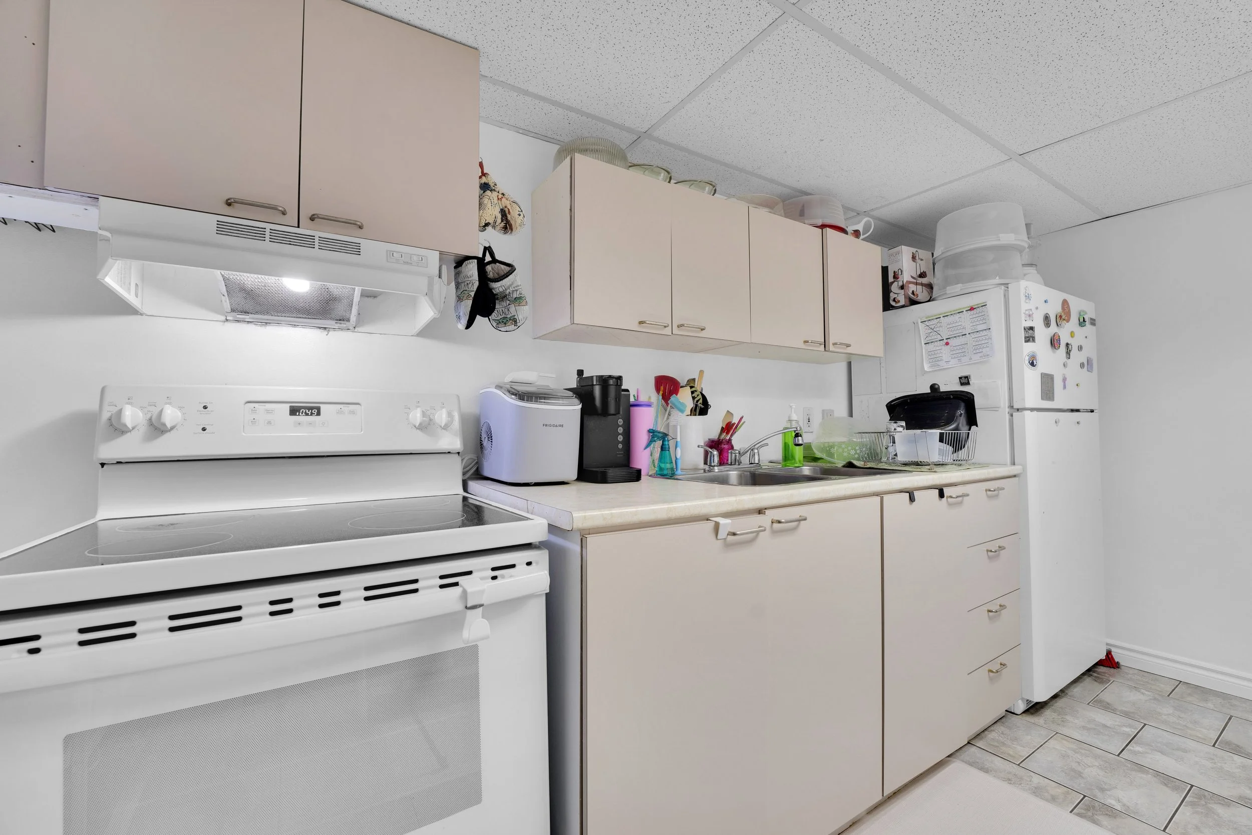 Ottawa Real Estate Media Services  A kitchen with white appliances, beige cabinets, and various kitchen items on the countertops.