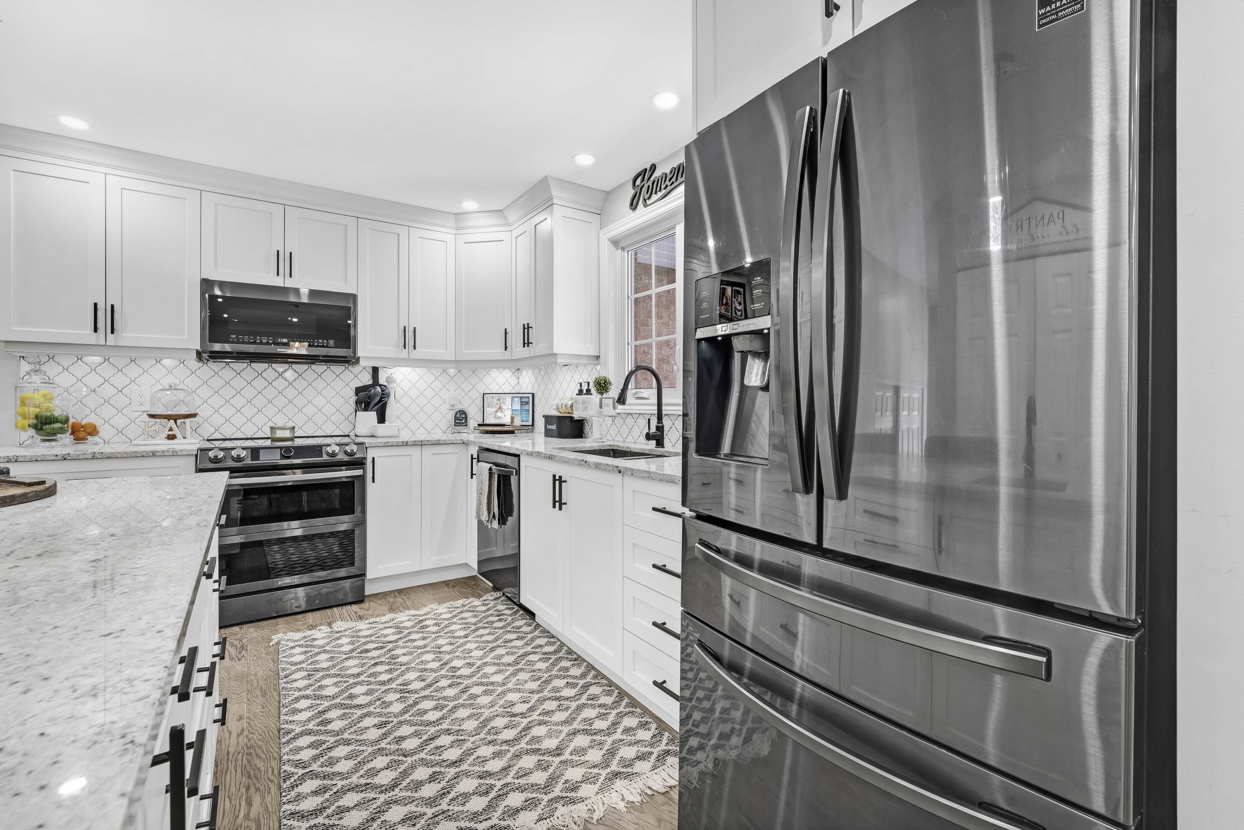 Real Estate Photography in Ottawa Modern kitchen with white cabinets, stainless steel appliances, and a patterned rug on wooden floor.