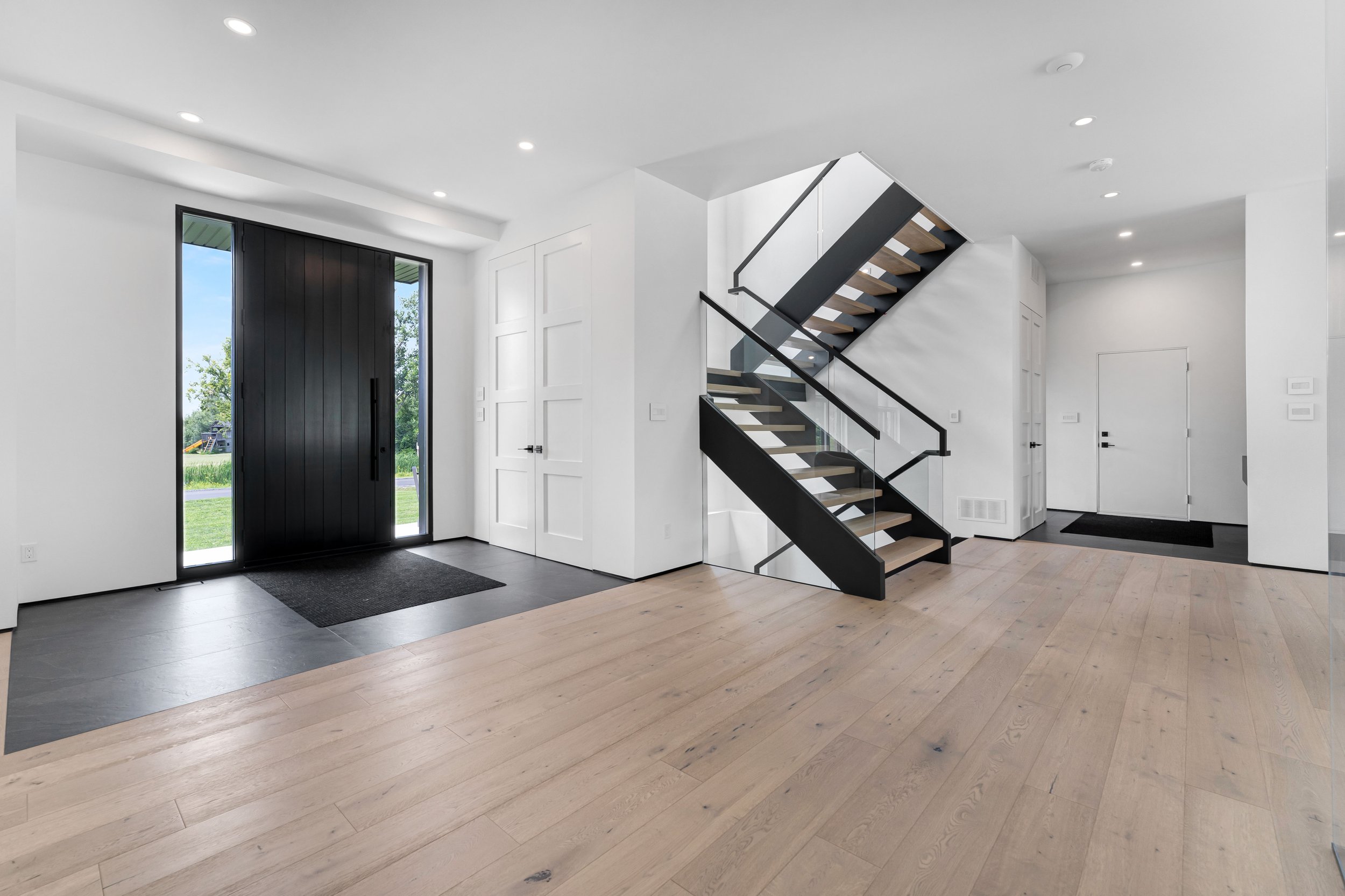 Modern entryway with a large wooden door, light wood flooring, and a contemporary staircase with glass railings. Real estate photography ottawa