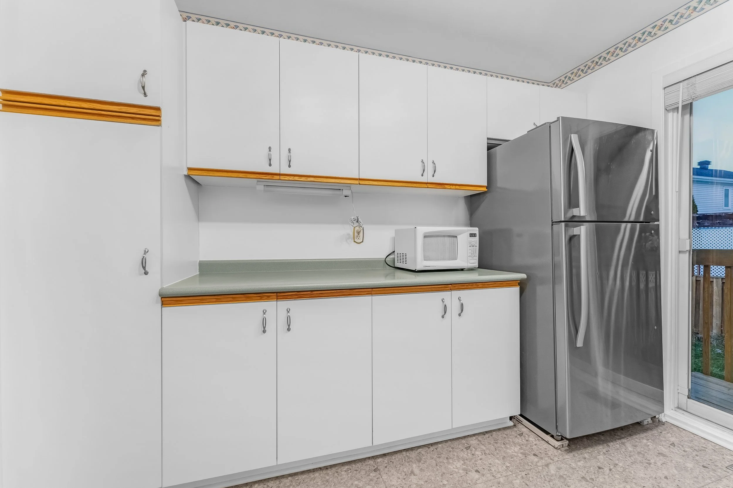 Kitchen with white cabinets, green countertop, microwave, and stainless steel refrigerator near sliding glass door.