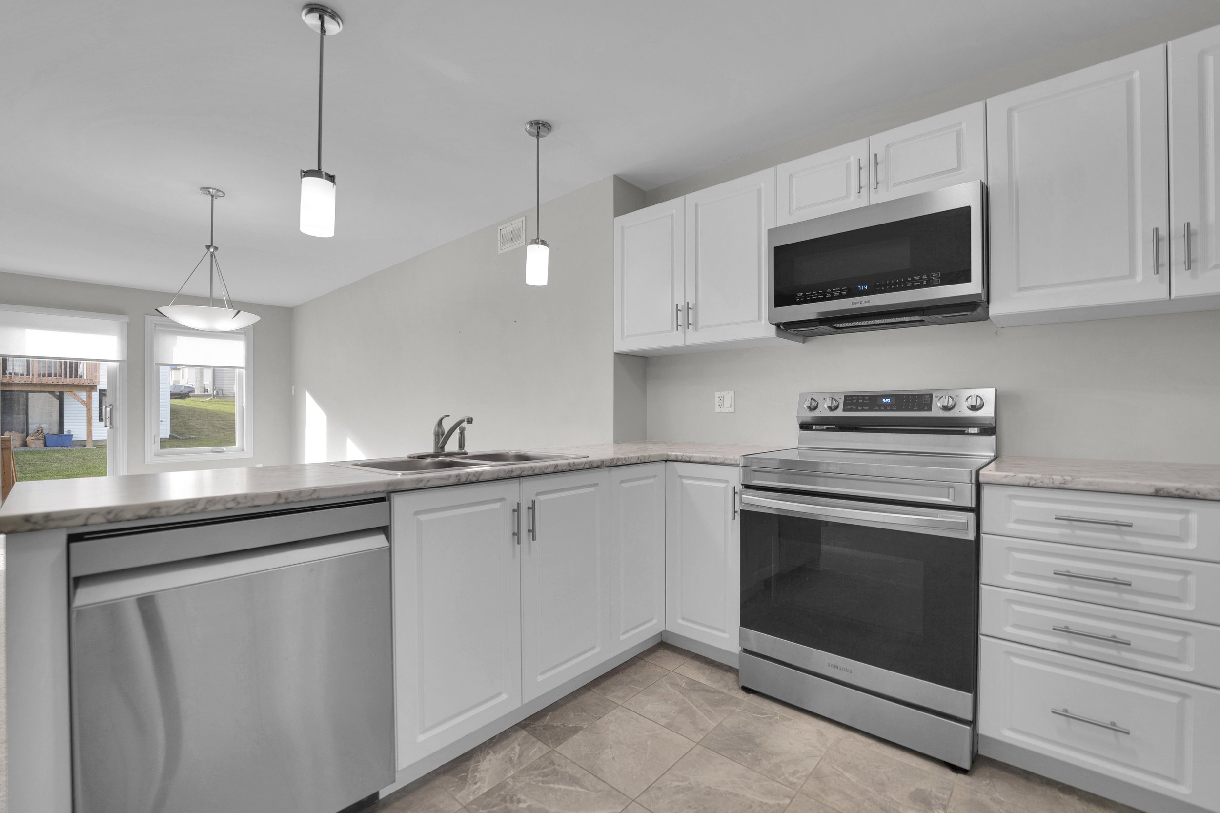 NVISION3D Real Estate Photography Ottawa  Modern kitchen with white cabinets, stainless steel stove and microwave, marble countertop, tiled floor, and large window with view of a backyard.