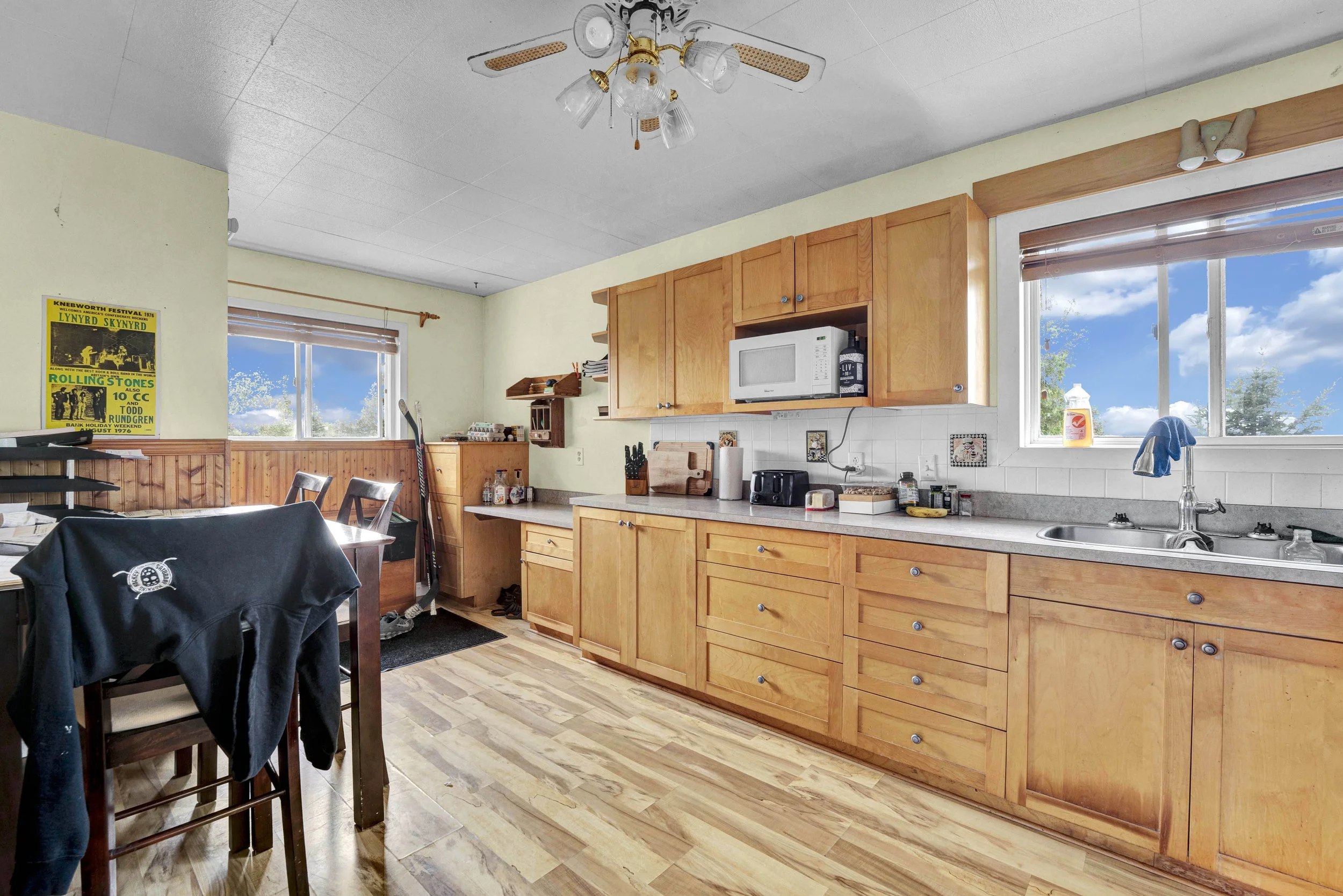 A kitchen with wooden cabinetry, a microwave, and windows showing a blue sky with clouds outside.