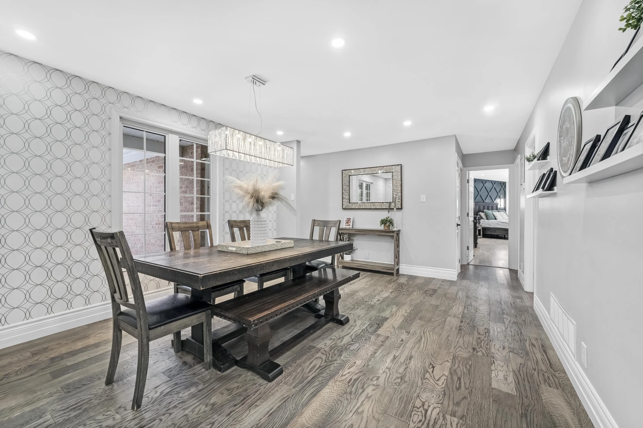 Ottawa Real Estate Photography  Modern dining room with wooden table, chairs, and a bench, decorated with a white vase and pampas grass, with large windows and wall art.