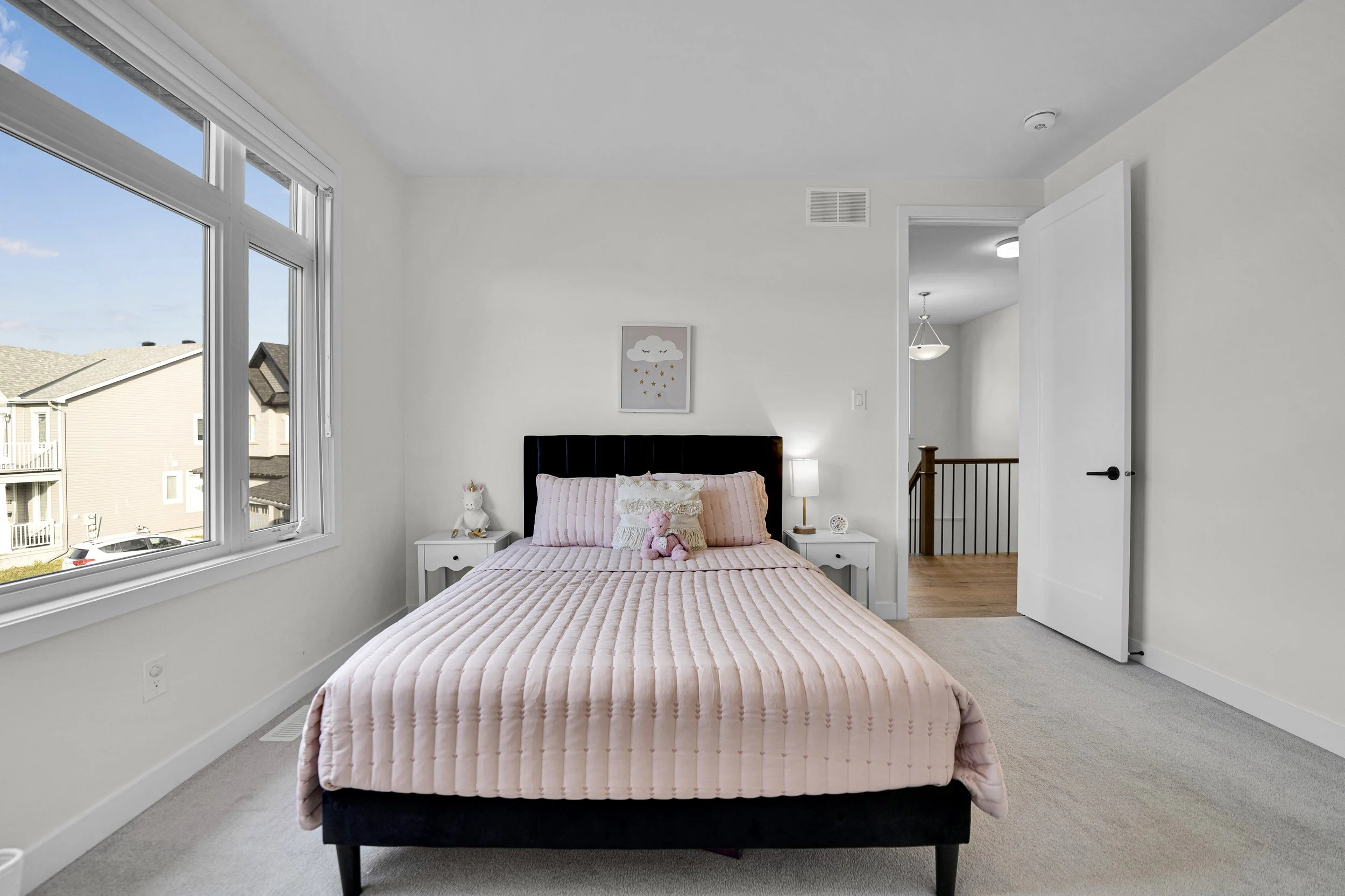 NVISION3D Real Estate Photography Ottawa  Bedroom with a large window, white walls, a bed with a pink quilt, stuffed animals, and nightstands with lamps.