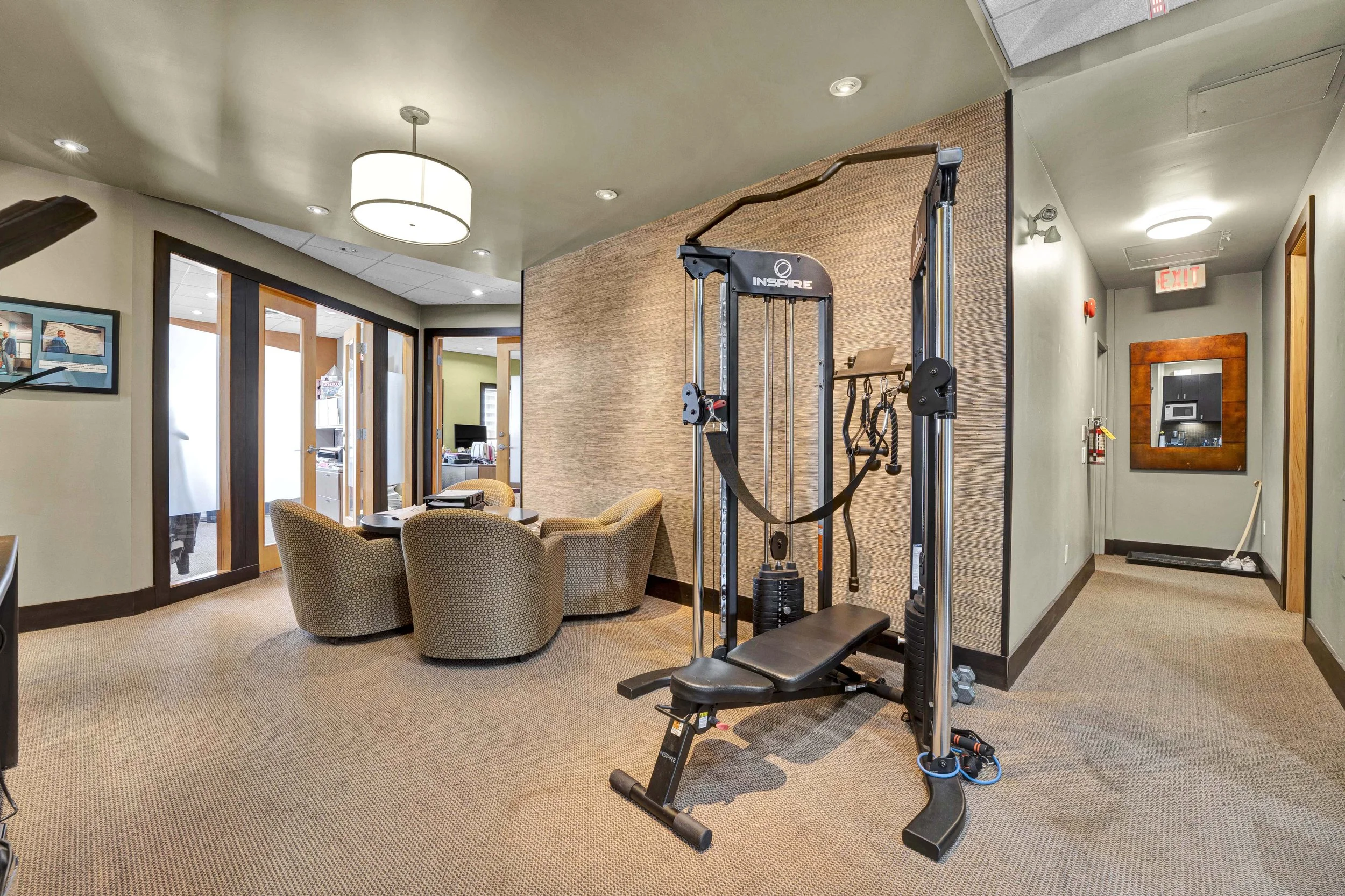 Ottawa Real Estate Photographer NVISION3D.ca  Interior of a health or fitness office with a seated area, a fitness machine, and a hallway with doors and fire safety equipment.