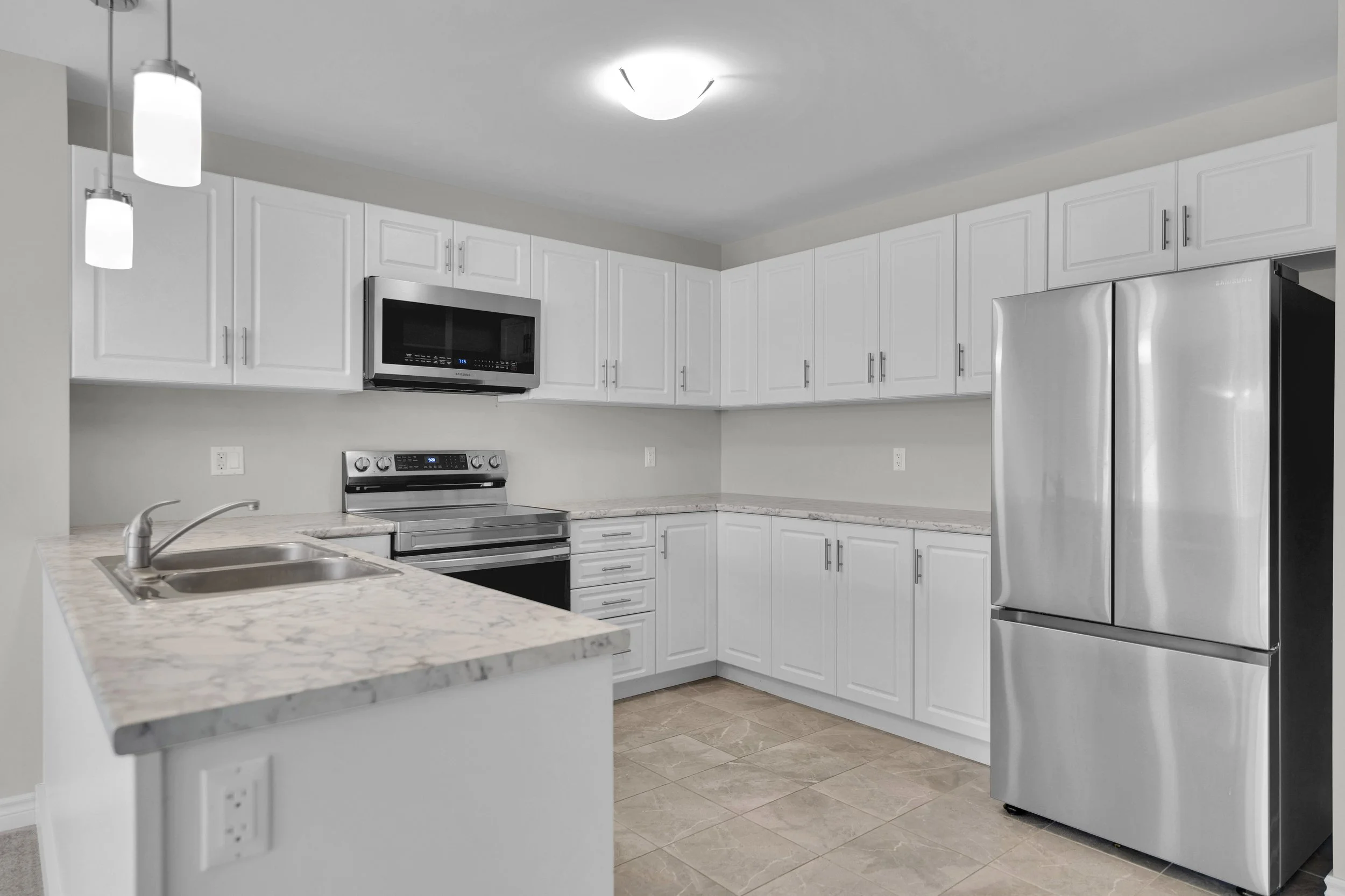 NVISION3D Real Estate Photography Ottawa  A modern kitchen with white cabinets, stainless steel appliances including a microwave, oven, and refrigerator, a granite countertop with an integrated sink, and pendant and ceiling lighting fixtures.