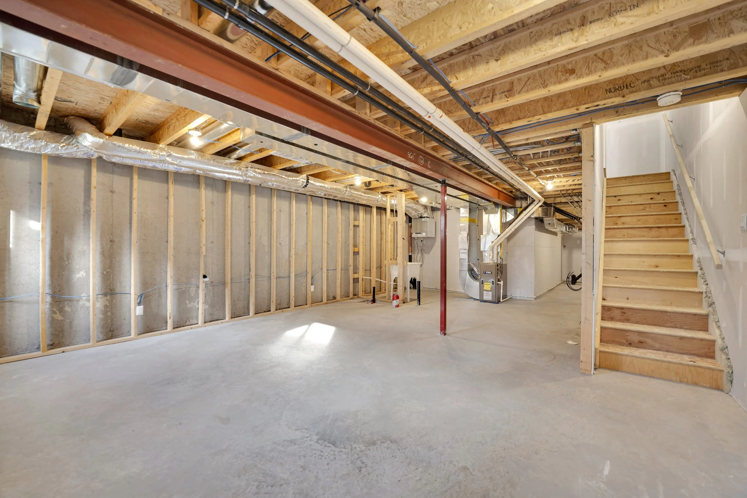 NVISION3D Real Estate Photography Ottawa  Interior view of a basement under construction with exposed ceiling beams, insulation, pipes, ductwork, and stairs leading to upper level.