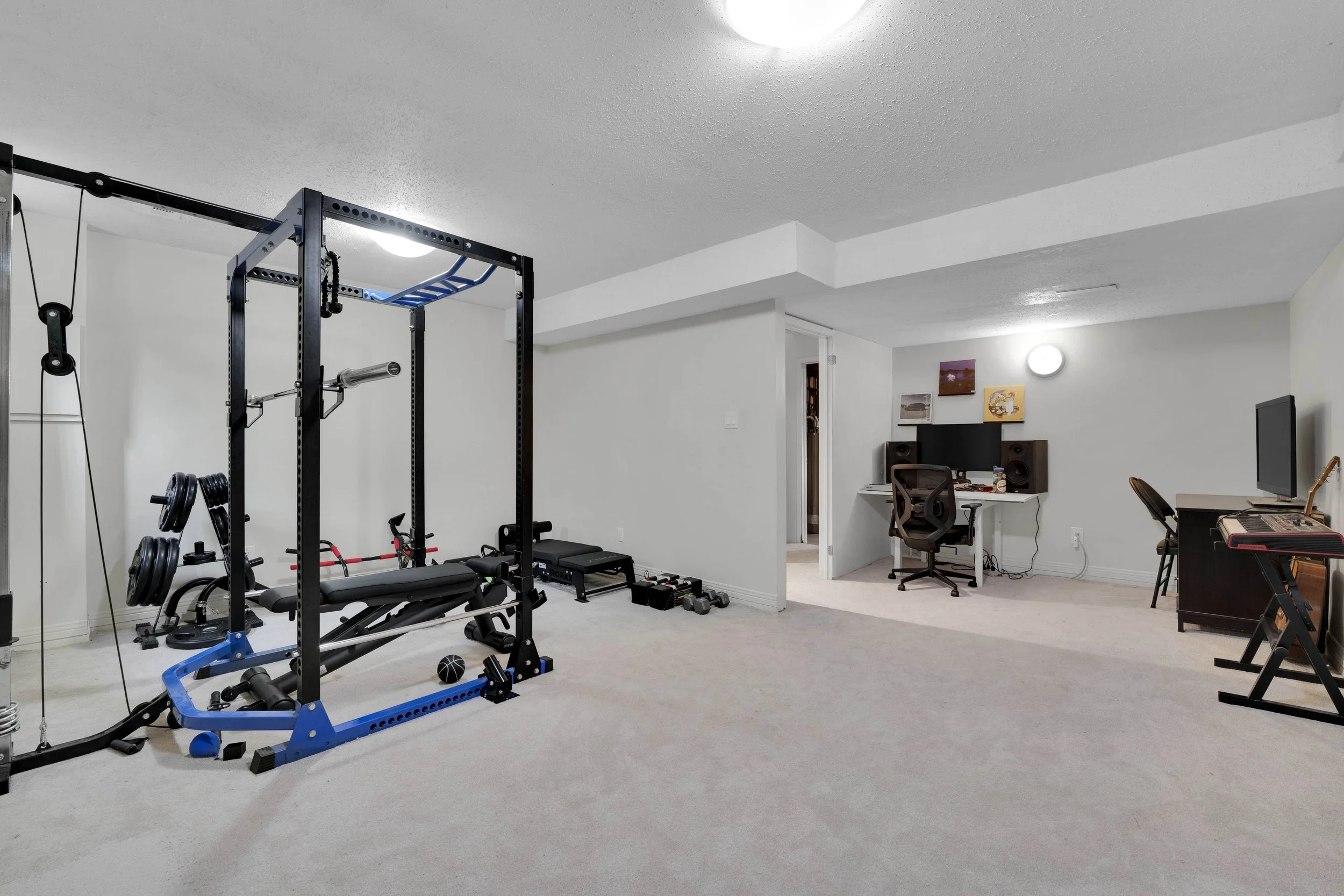 Home gym area with weight lifting equipment and a computer workspace in a basement.