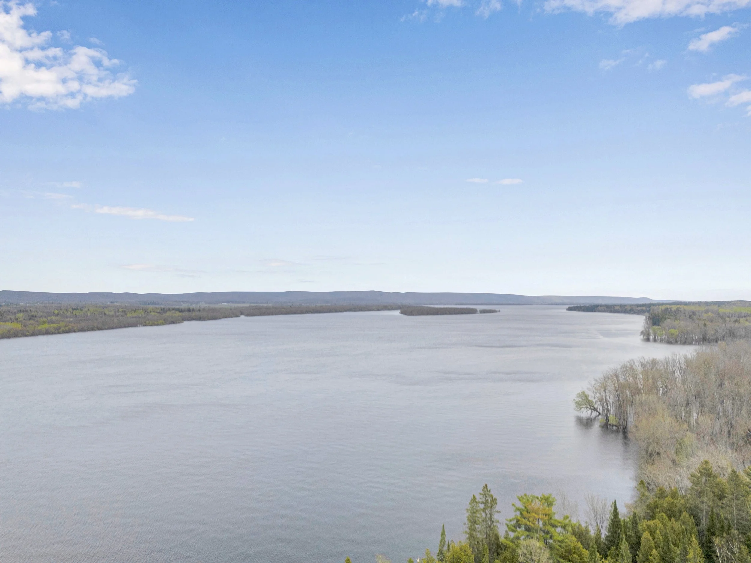 Ottawa Real Estate Media Services  A large body of water, possibly a lake or river, with distant shoreline and hills under a blue sky with some scattered clouds.