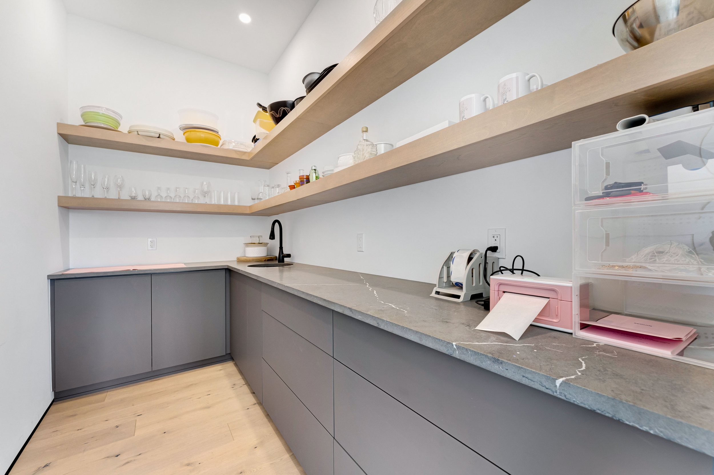 Modern pantry with open shelves, gray cabinets, and countertop containing kitchenware, glassware, and storage containers.
