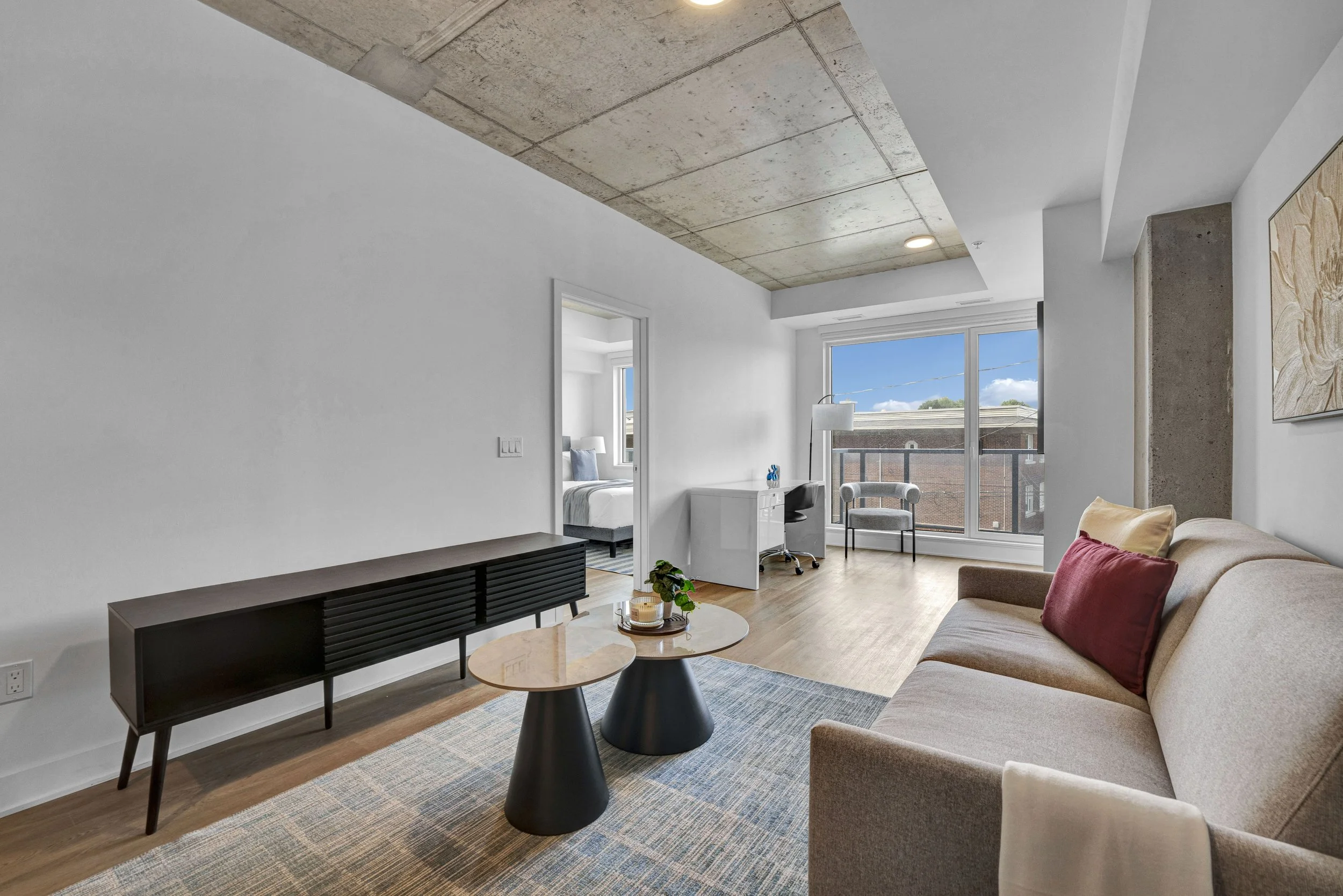Ottawa Real Estate NVISION 3D  Living room with beige sofa, red pillow, black coffee tables, floral artwork, wooden floors, large window, and city view.