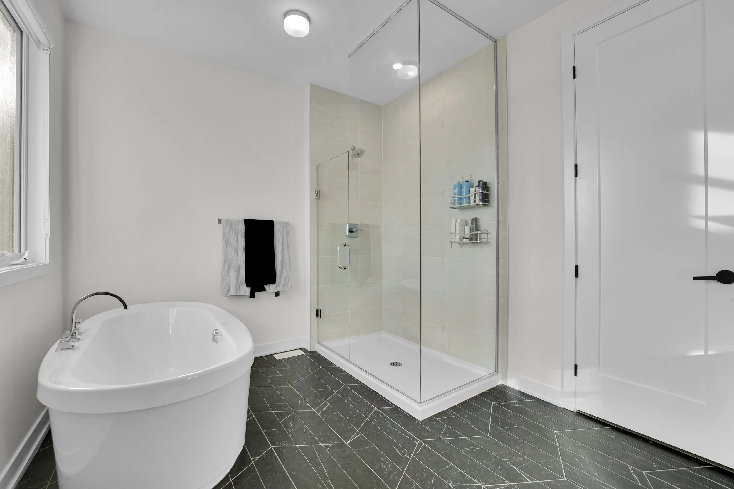 NVISION3D Real Estate Photography Ottawa  Modern bathroom with a walk-in glass shower, a freestanding bathtub, dark gray tiled floor, and white walls. Natural light coming through a window.